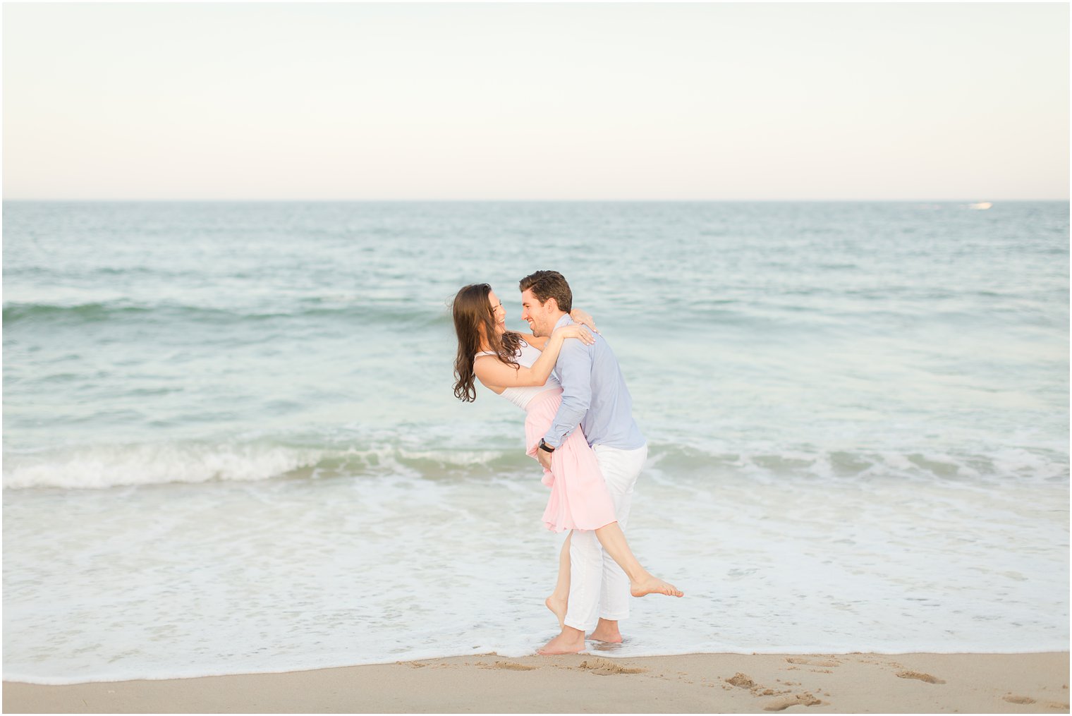 bride and groom play in the ocean during engagement session in Spring Lake