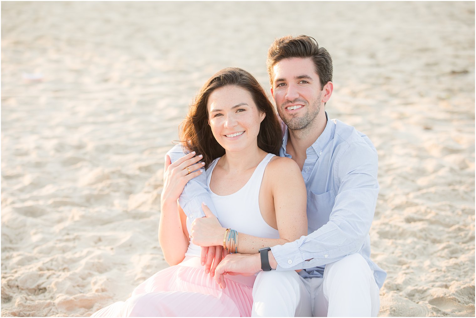 groom hugs bride while sitting on beach in New Jersey
