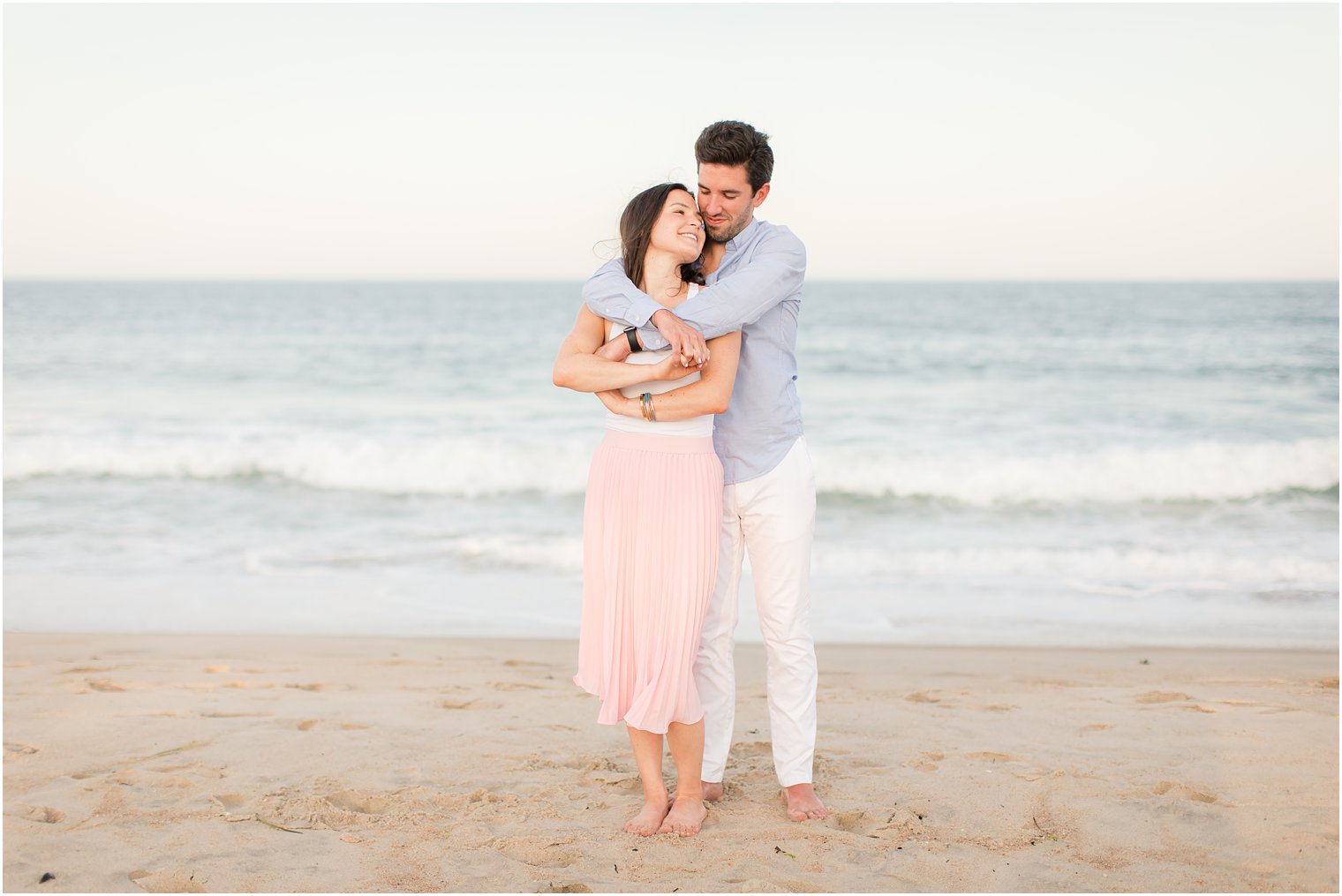 groom hugs bride while standing on sand at Spring Lake beach