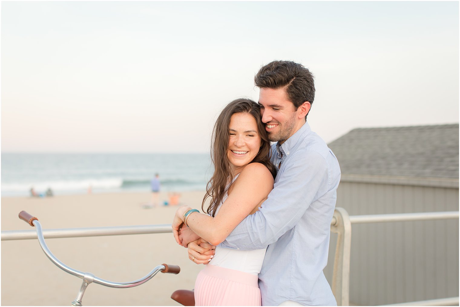 groom hugs bride from behind during Spring Lake engagement portraits on boardwalk