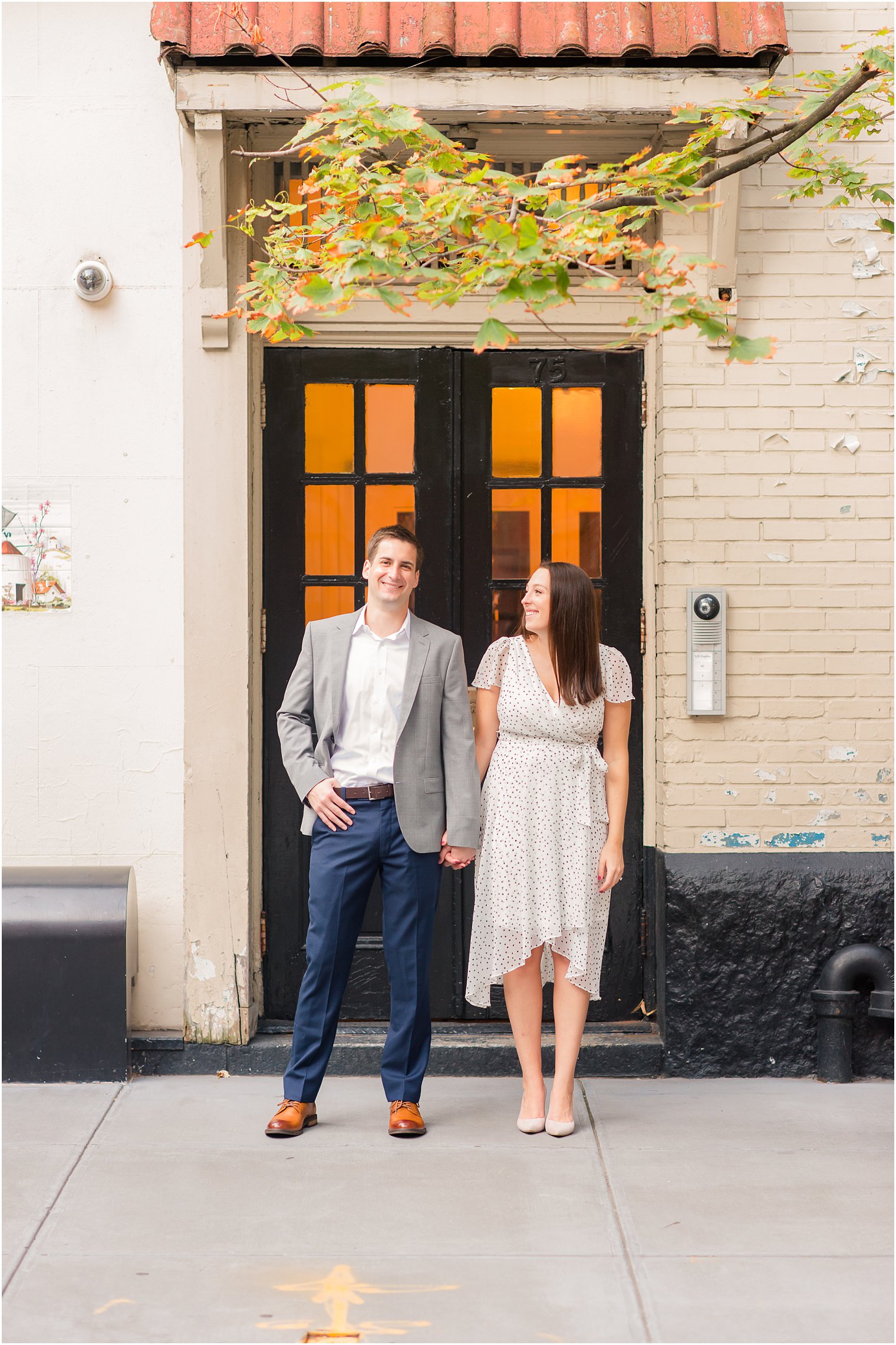 bride and groom hold hands outside West Village building during engagement session