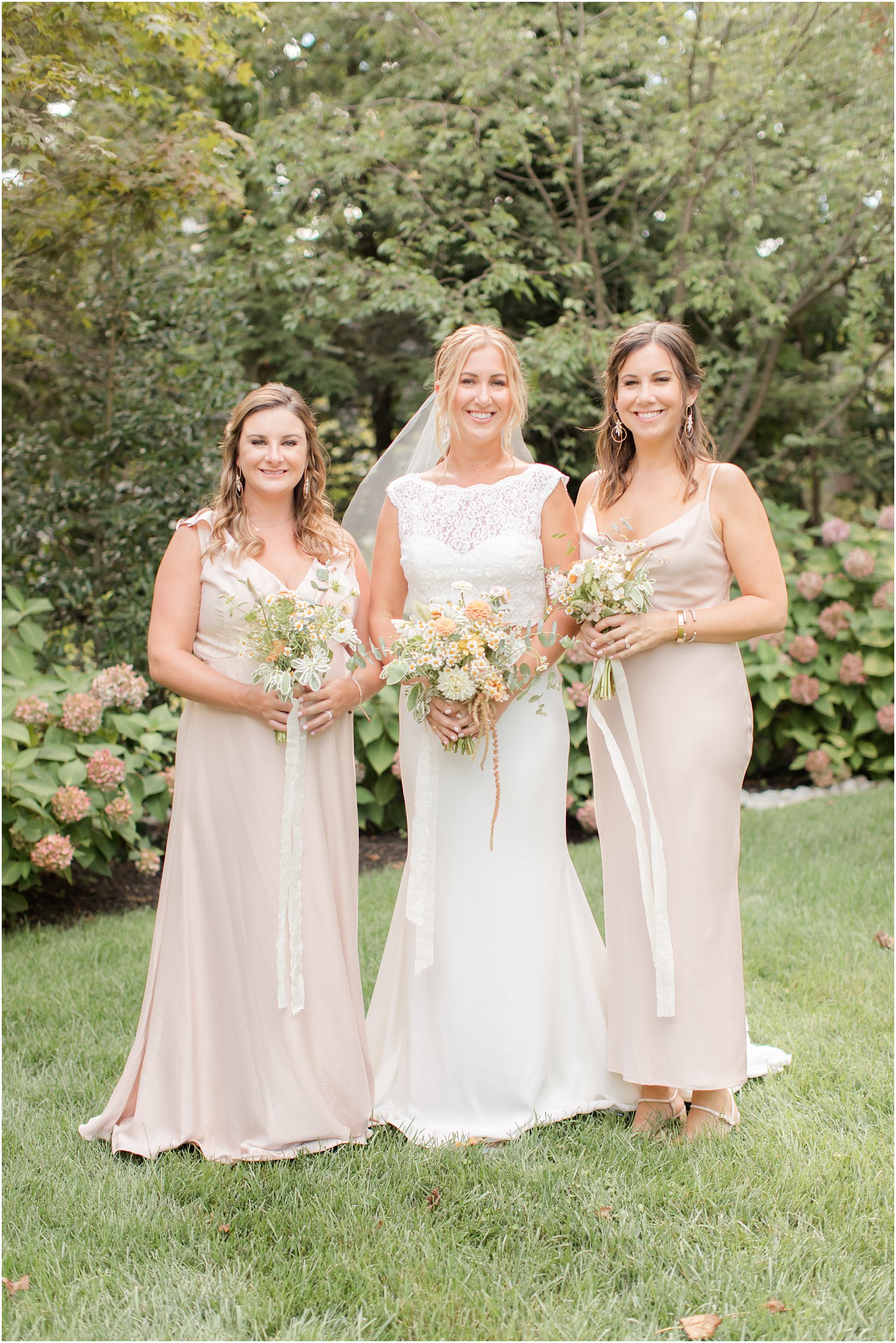 bride poses with 2 bridesmaids in pale pink gowns