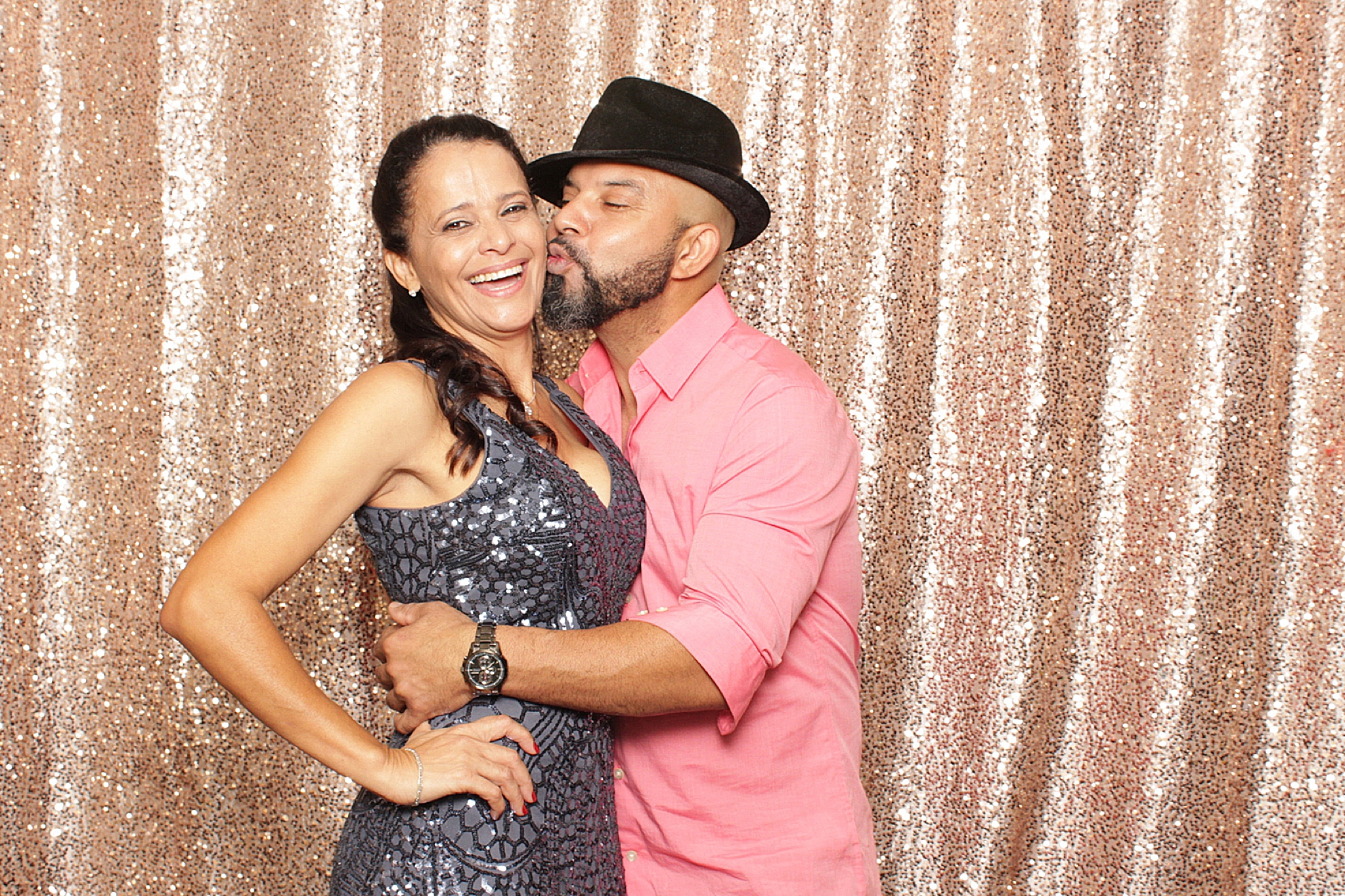 guests kiss in front of rose gold photo booth backdrop