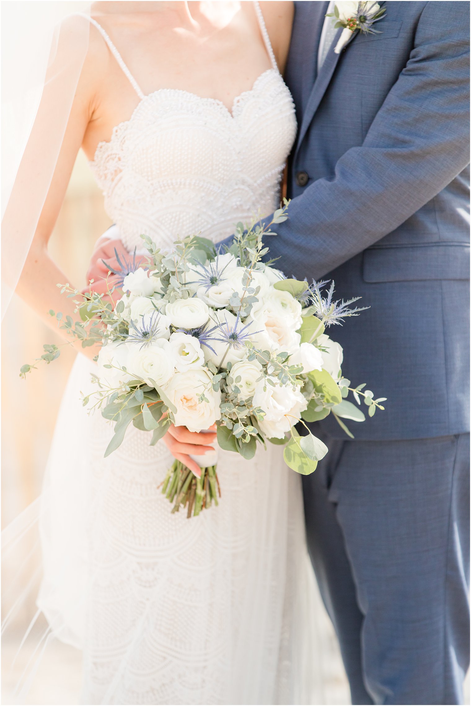 bride holds bouquet by hip while groom hugs her