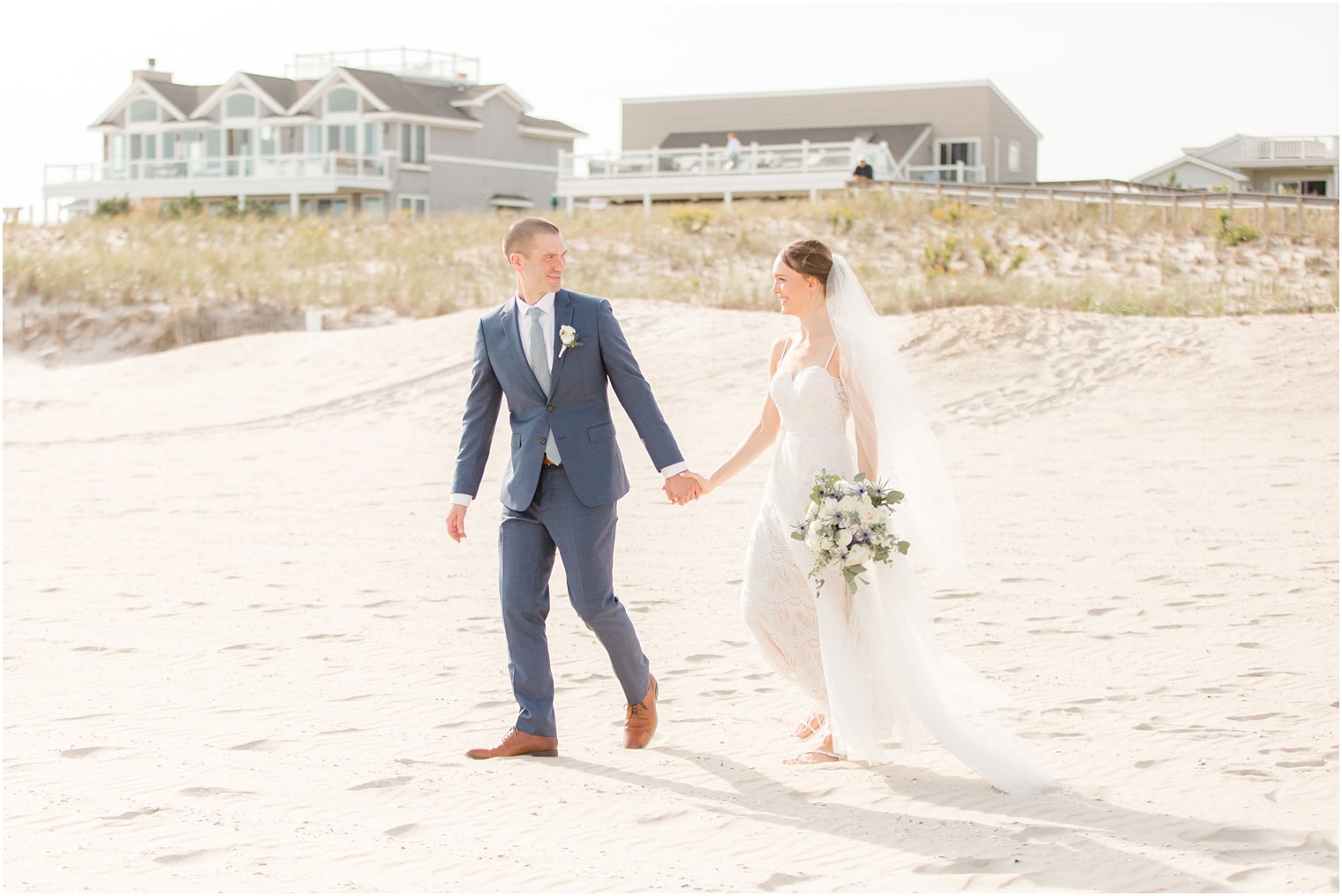bride and groom hold hands and walk along beach