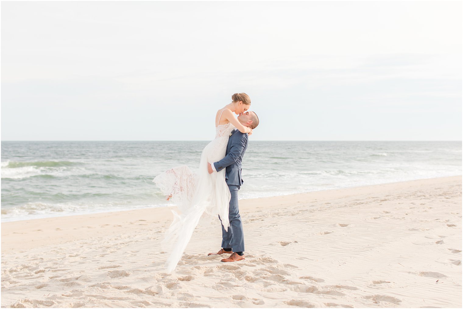 groom lifts bride up while kissing on beach