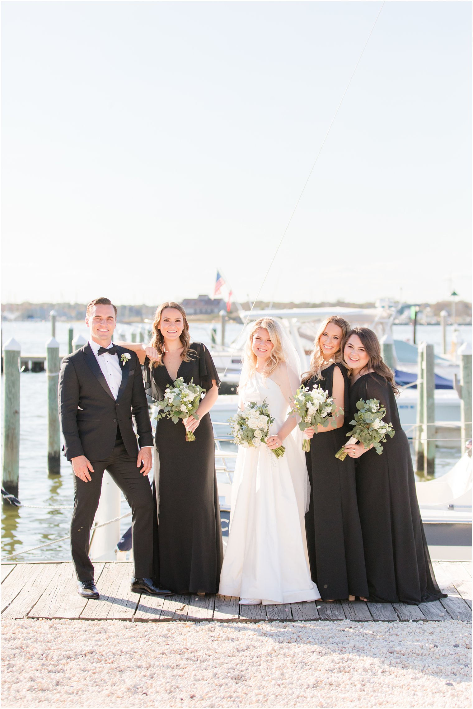 bride poses with bridal party on pier at Mantoloking Yacht Club