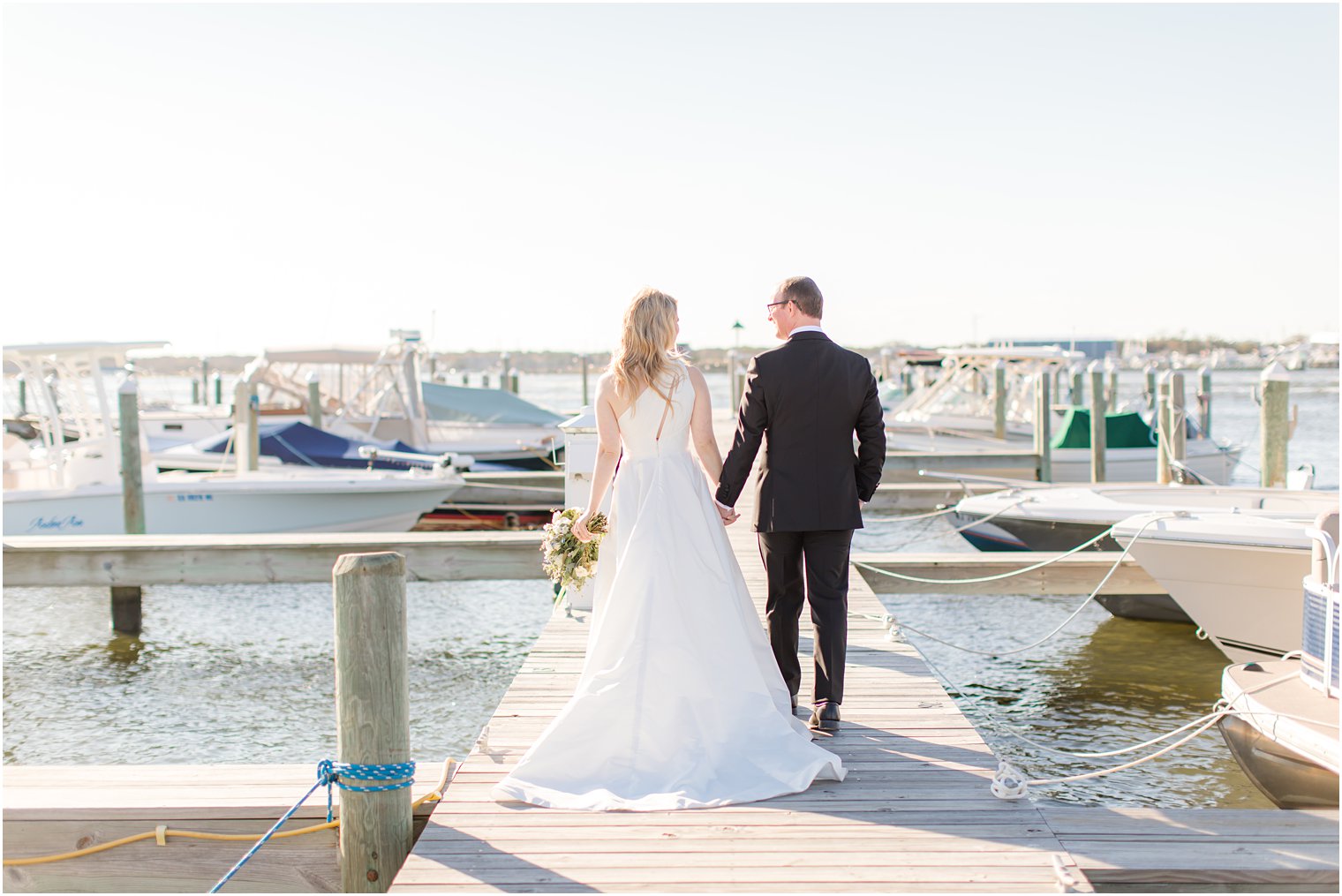 bride and groom walk along pier at Mantoloking Yacht Club