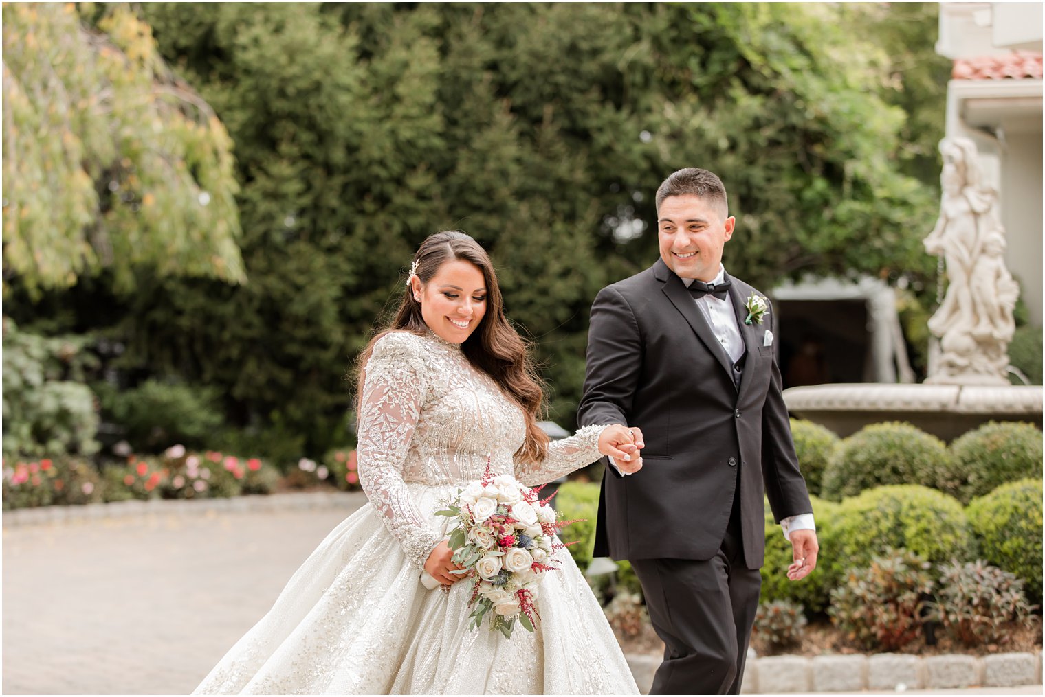 groom looks at bride while holding her hand and walking through garden