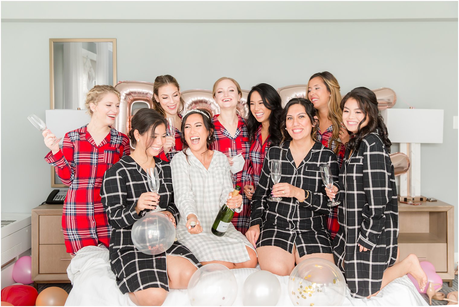 bride poses with bridesmaids on bed with balloons and champagne