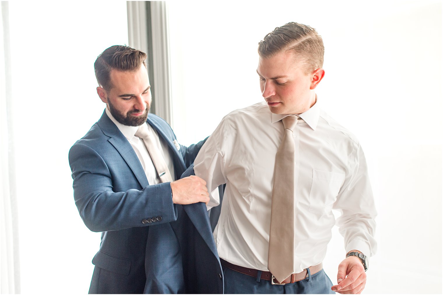 groom gets into jacket with help from groomsman before Seaview Hotel wedding