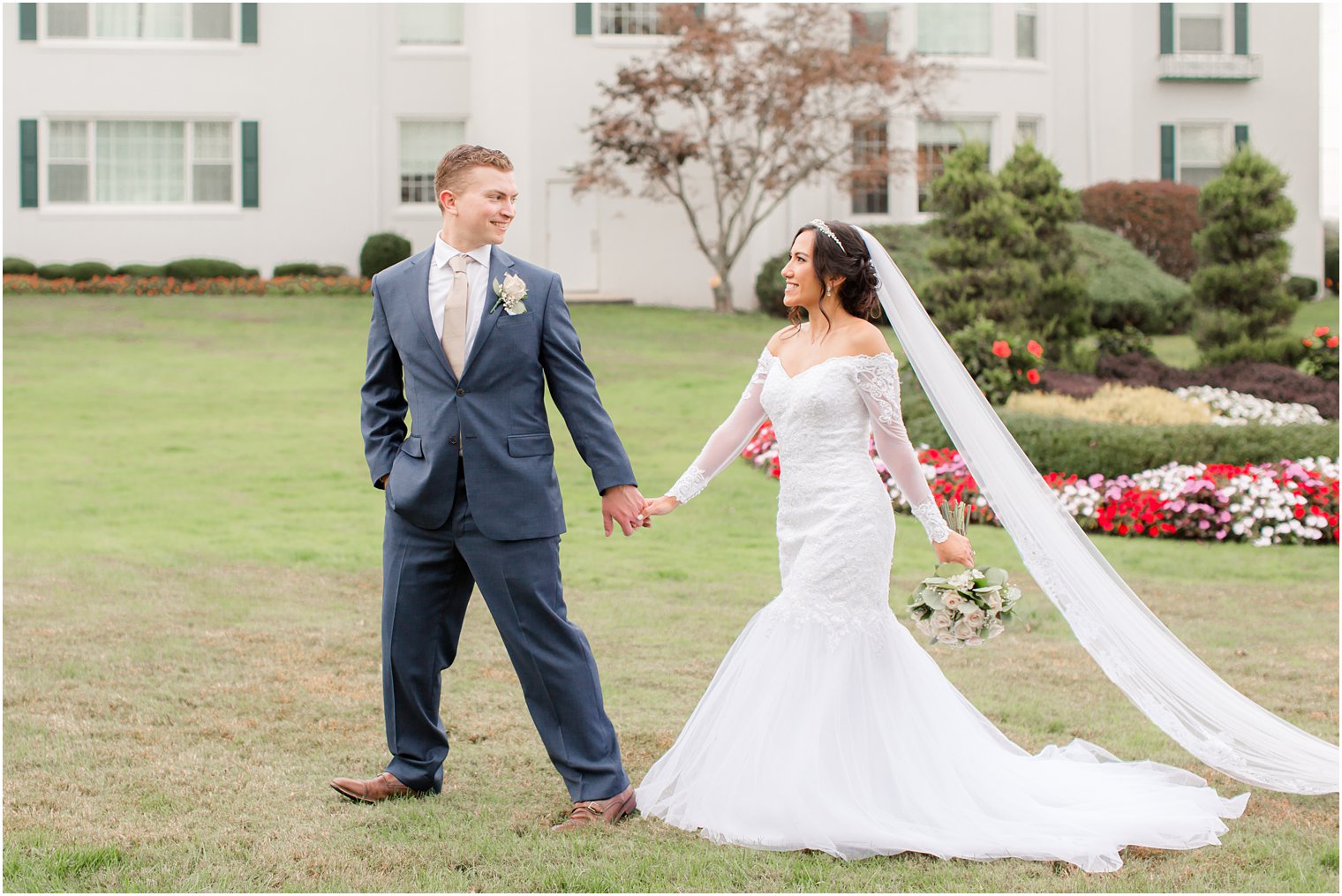 bride and groom walk along grounds of Seaview Hotel with bride's veil trailing