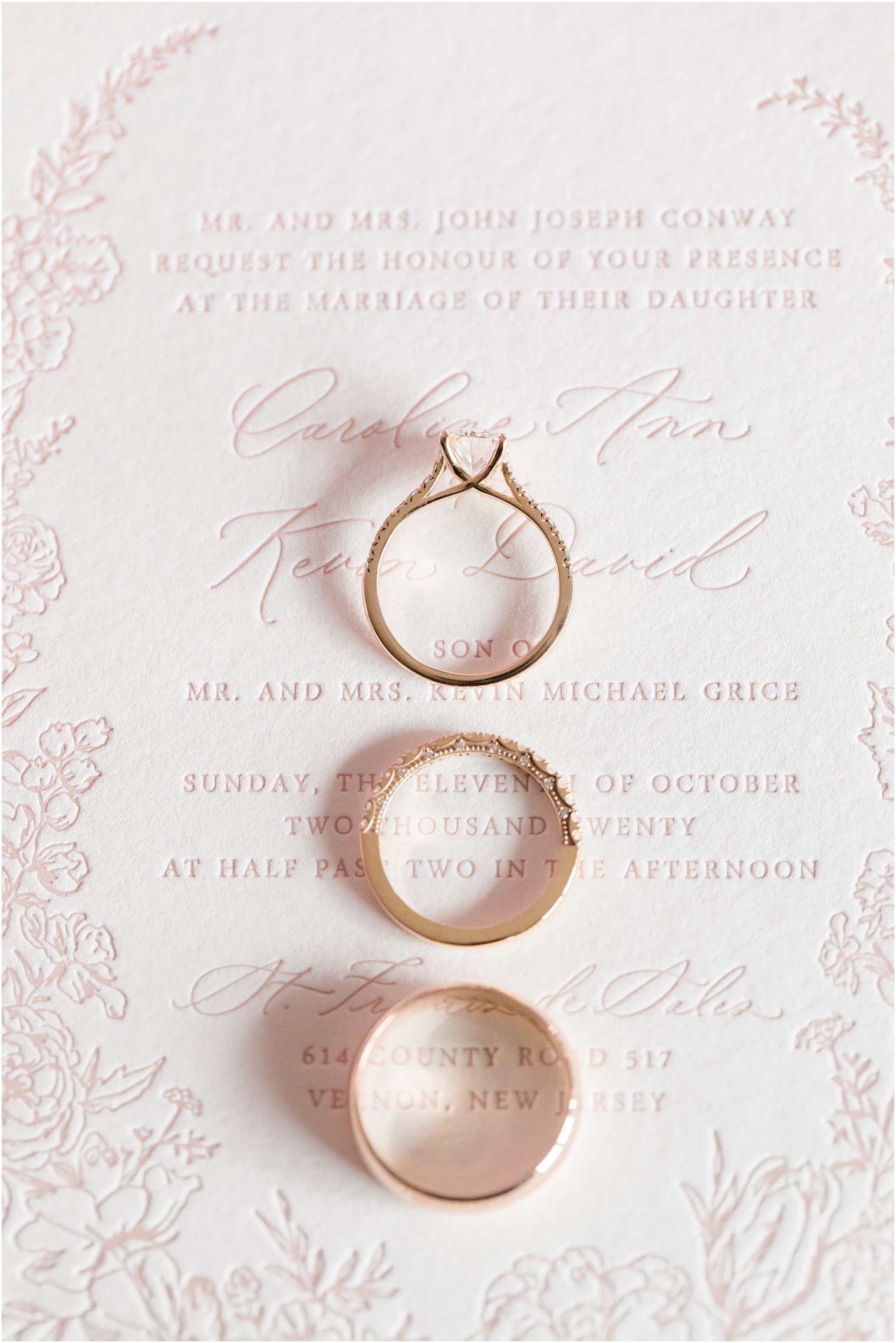 gold wedding bands sit on pink wedding invitation
