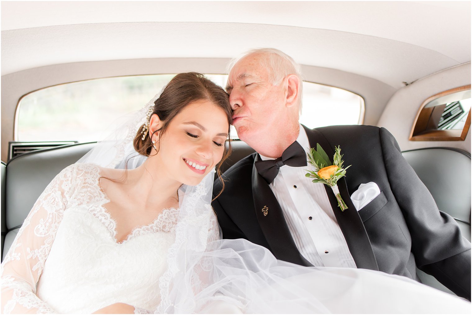 bride's father kisses her forehead in classic car before wedding