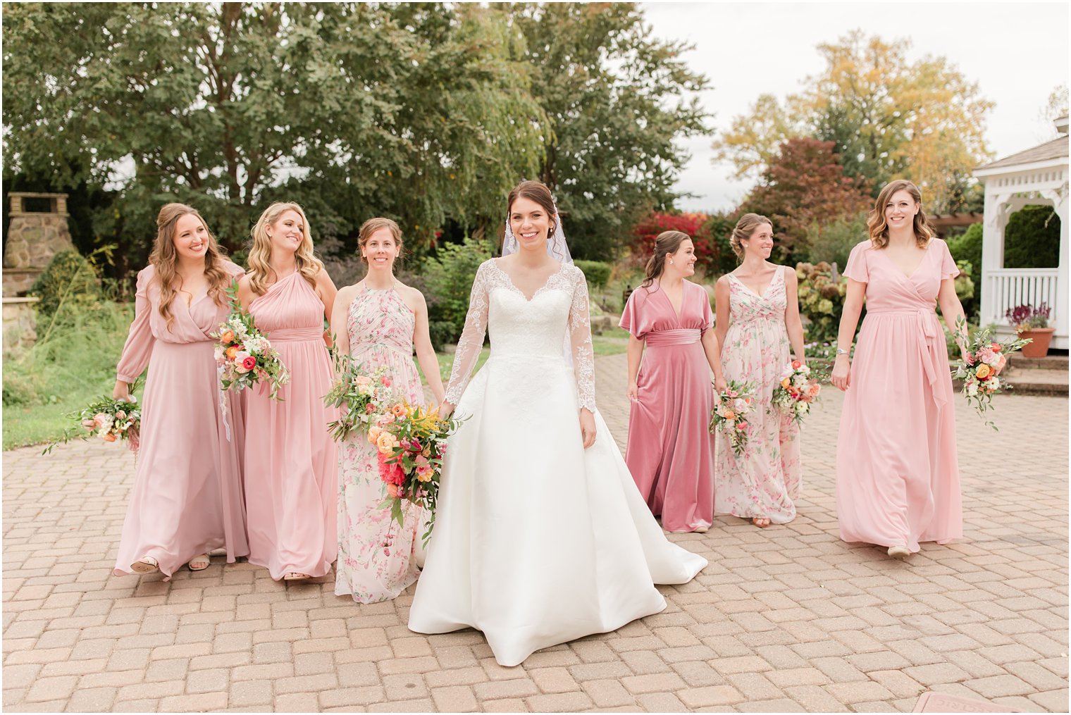 bride walks through gardens with bridesmaids in pink gowns