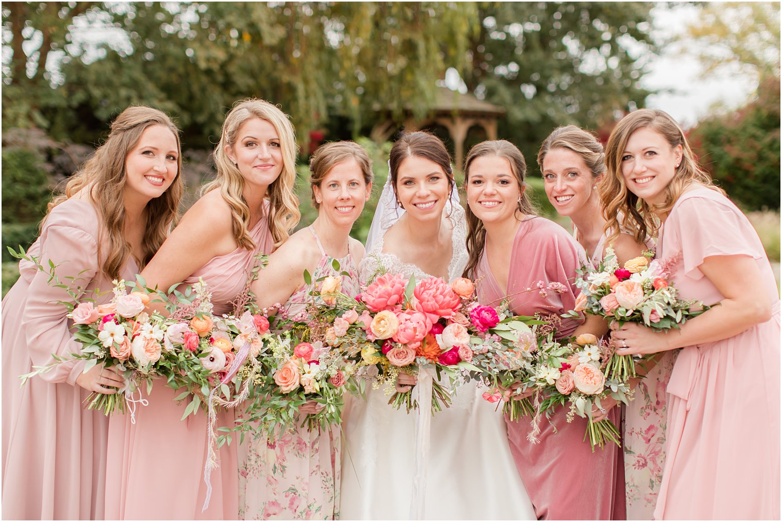 bridesmaids with mismatched pink gowns pose with bride
