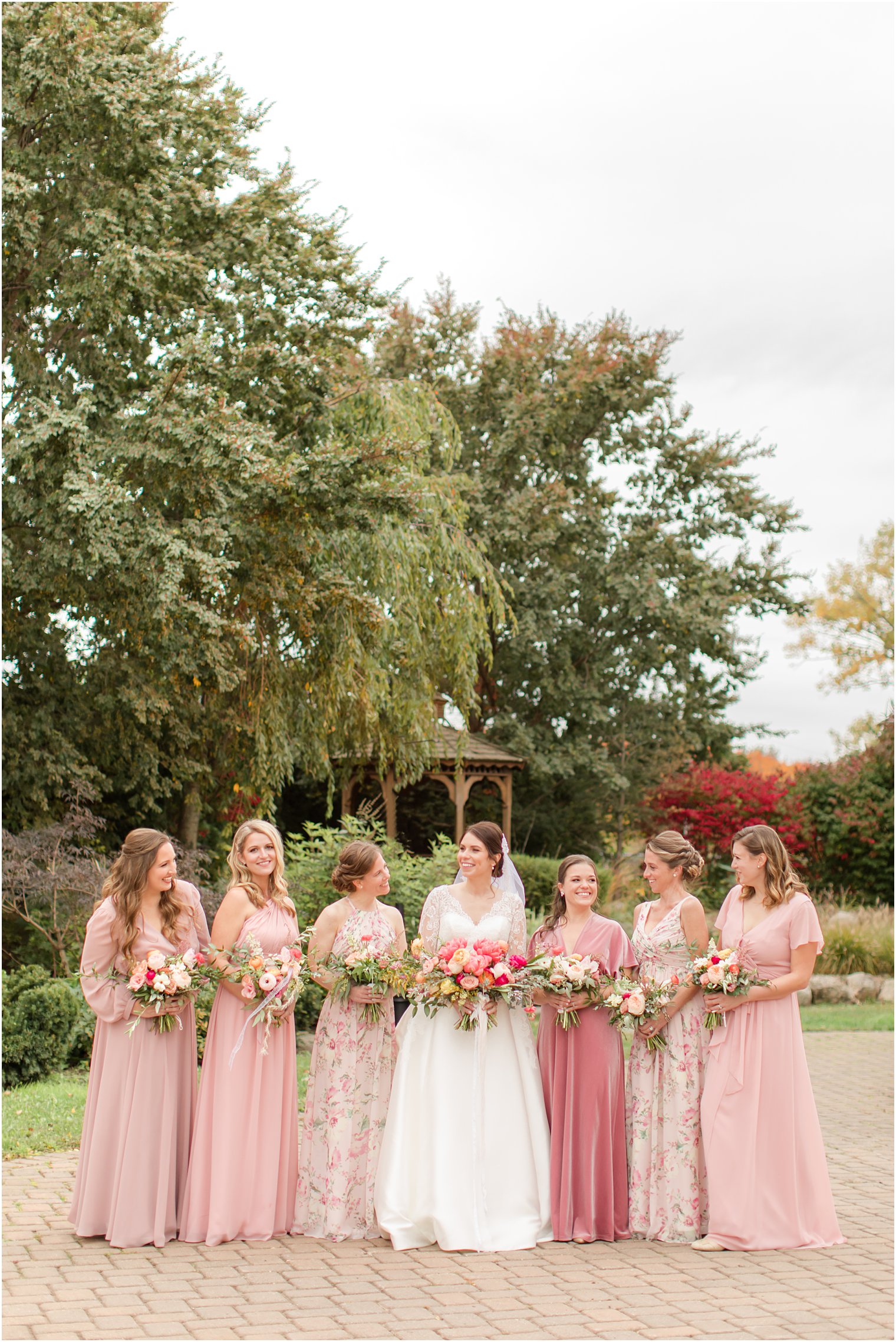 bride poses with bridesmaids in mismatched pink gowns