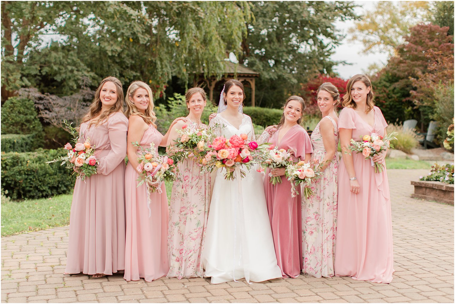 bridesmaids in mismatched pink gowns pose with bride