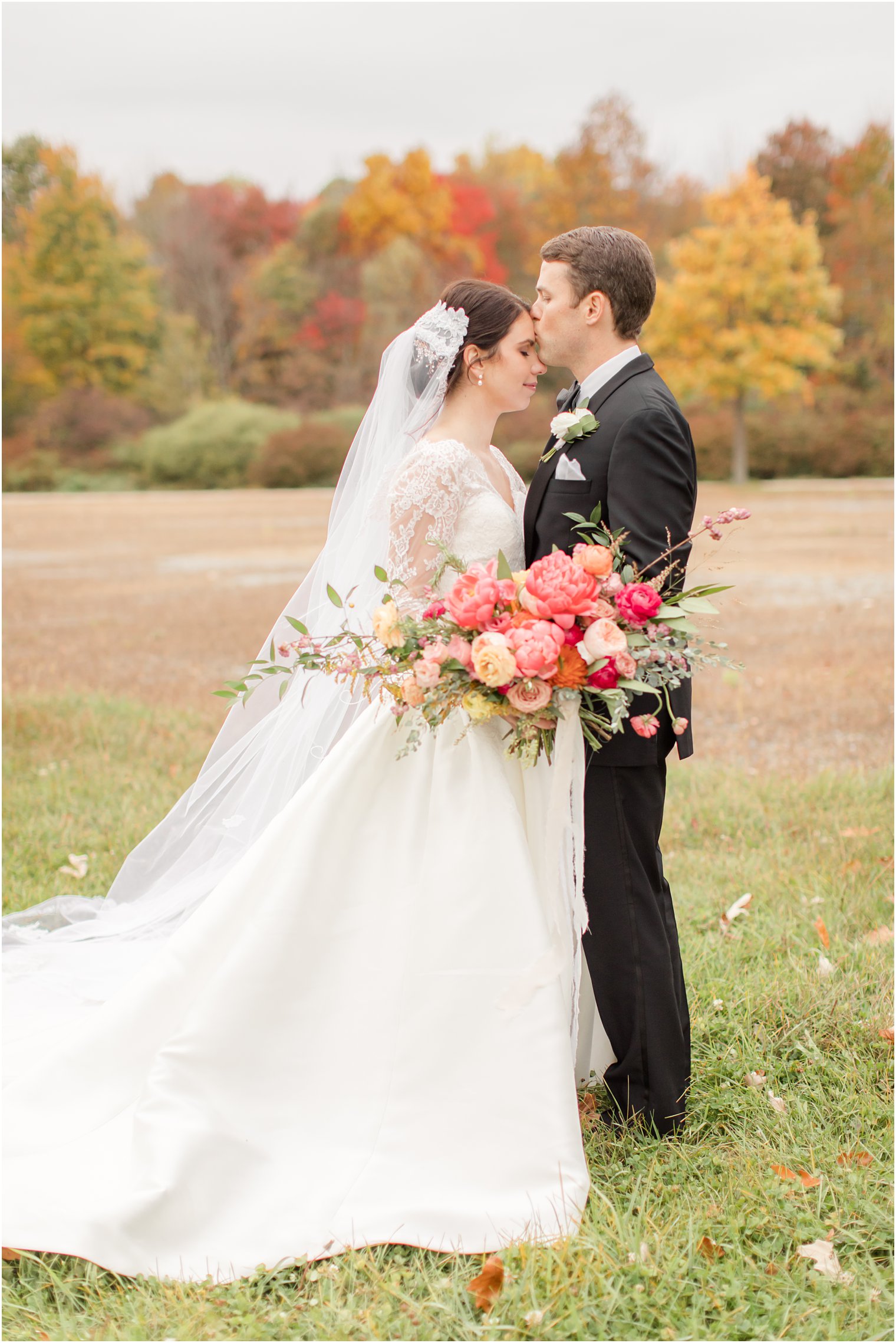 bride and groom stand in field during fall wedding portraits