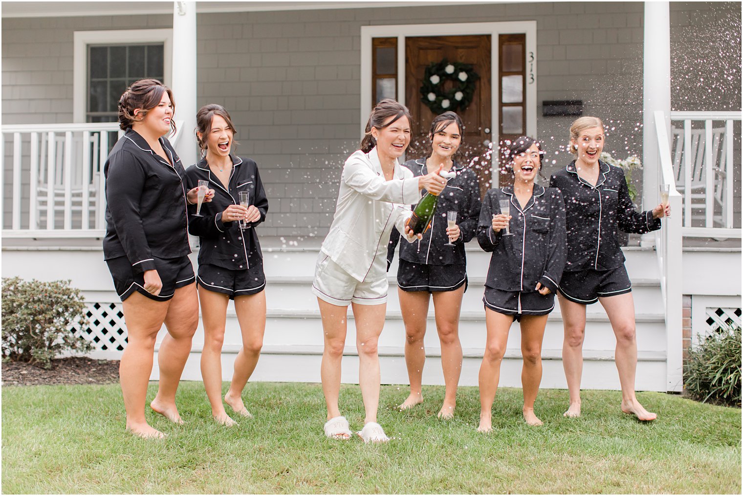 bride pops champagne on front lawn with bridesmaids before The Mill Lakeside Manor Wedding