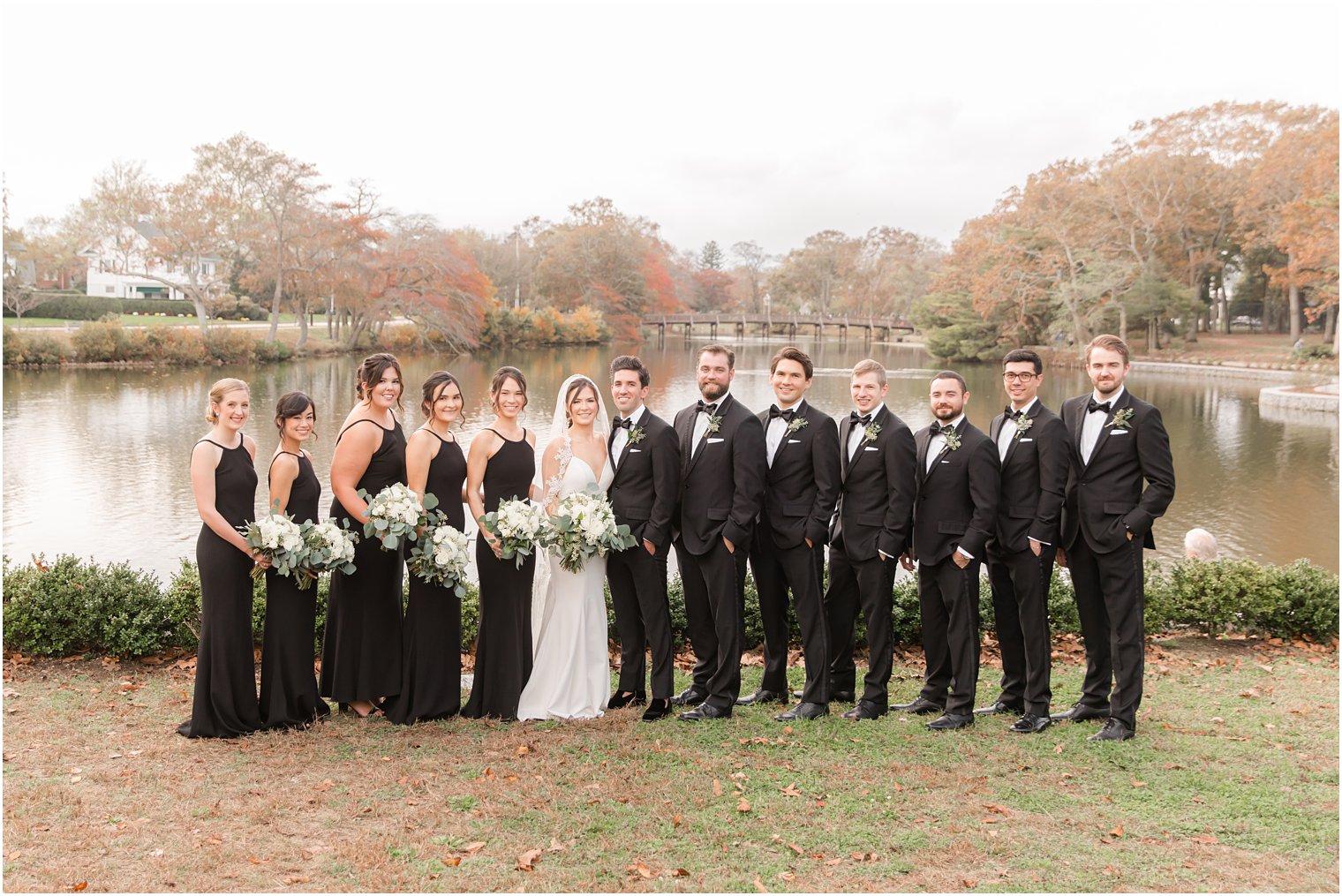 bridal party in black poses by lake in Divine Park