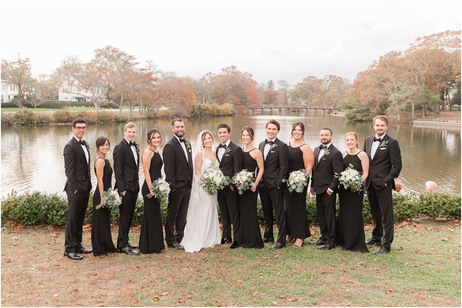 full bridal party poses by lake in Divine Park