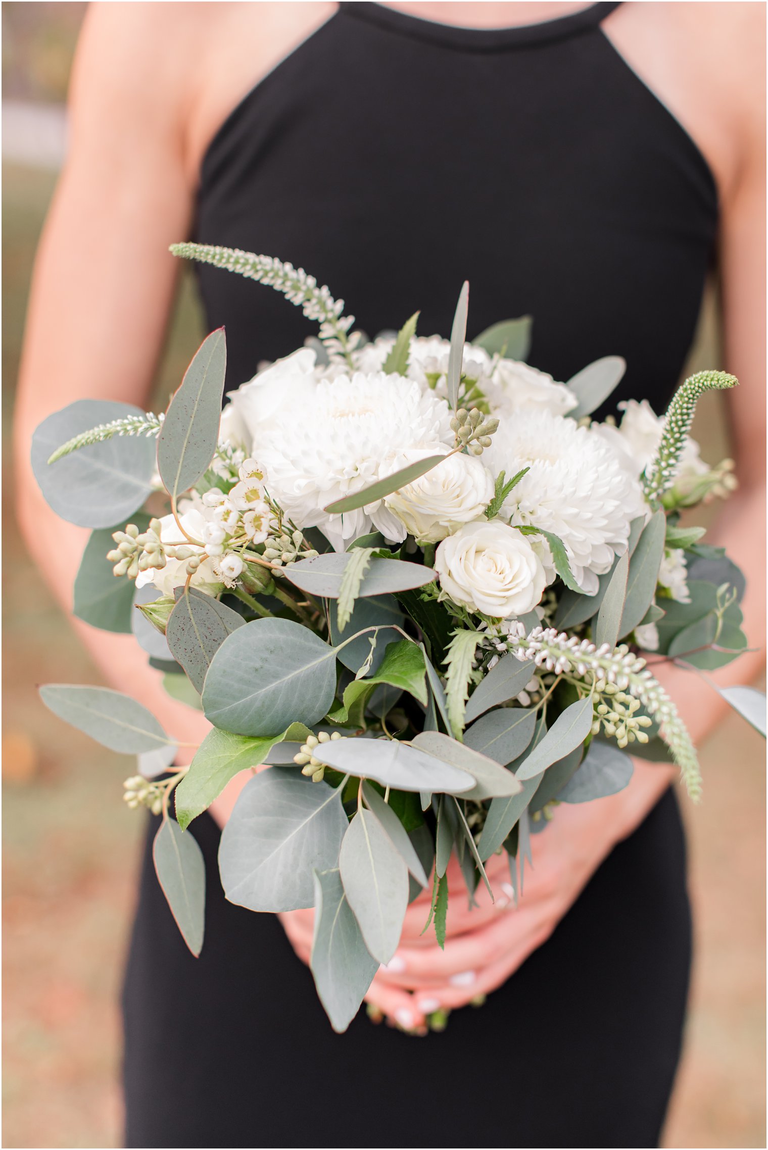 bridesmaid in black gown holds bouquet with white flowers and green accents