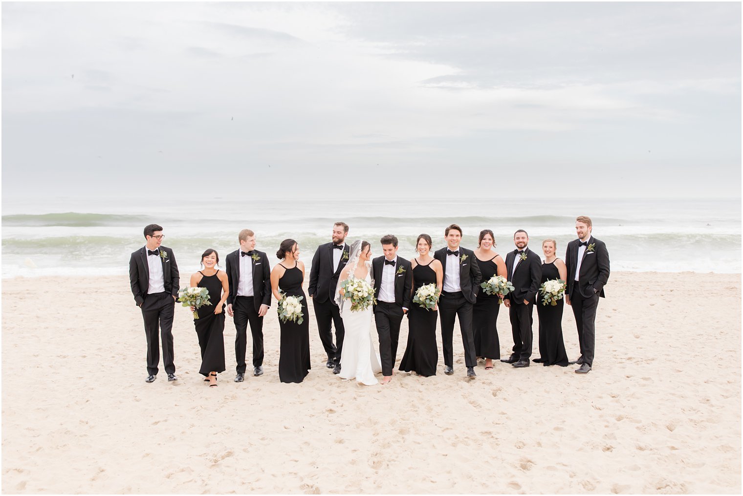 wedding party in black walks on Spring Lake Beach