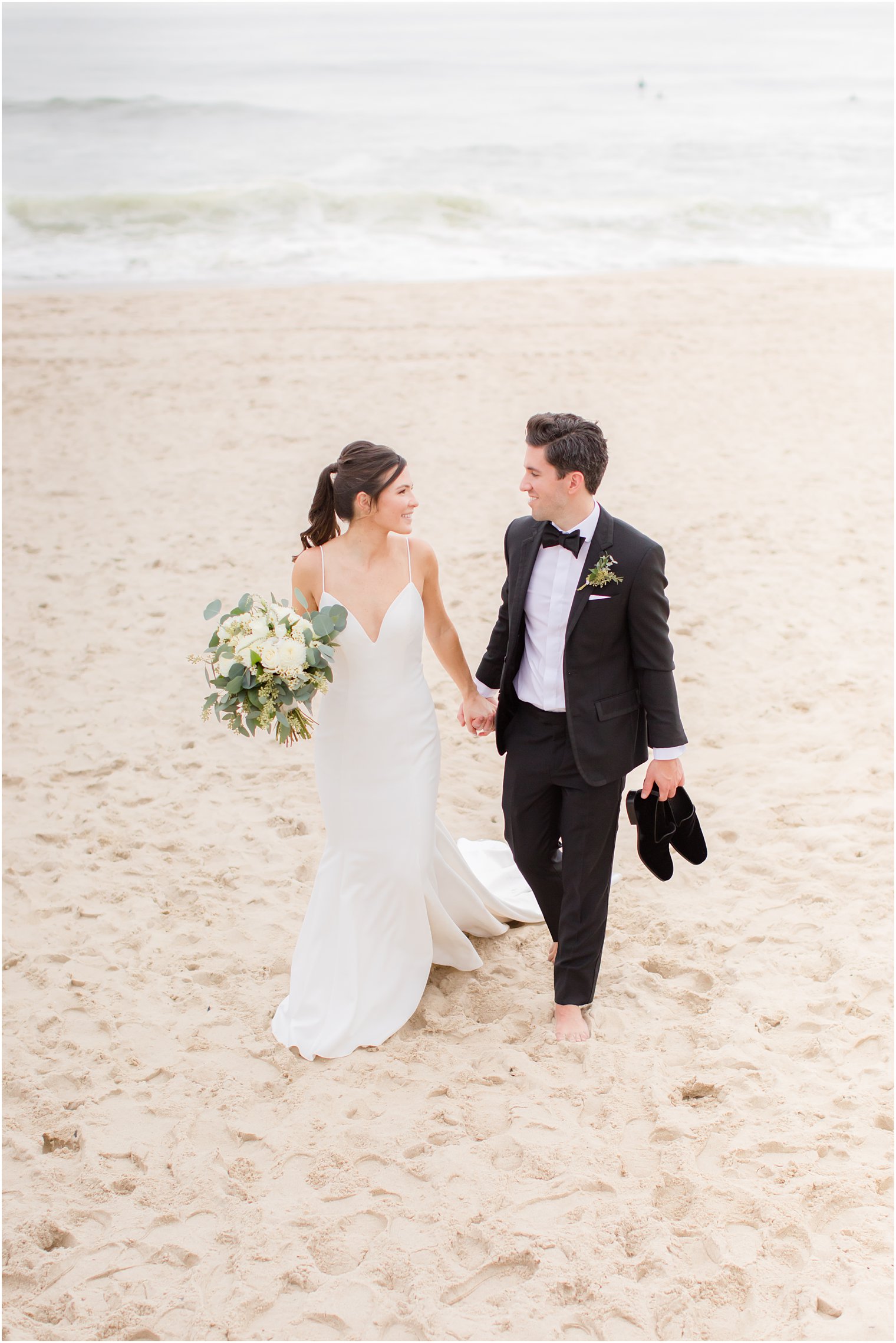 bride and groom hold hands walking through sand in Spring Lake NJ