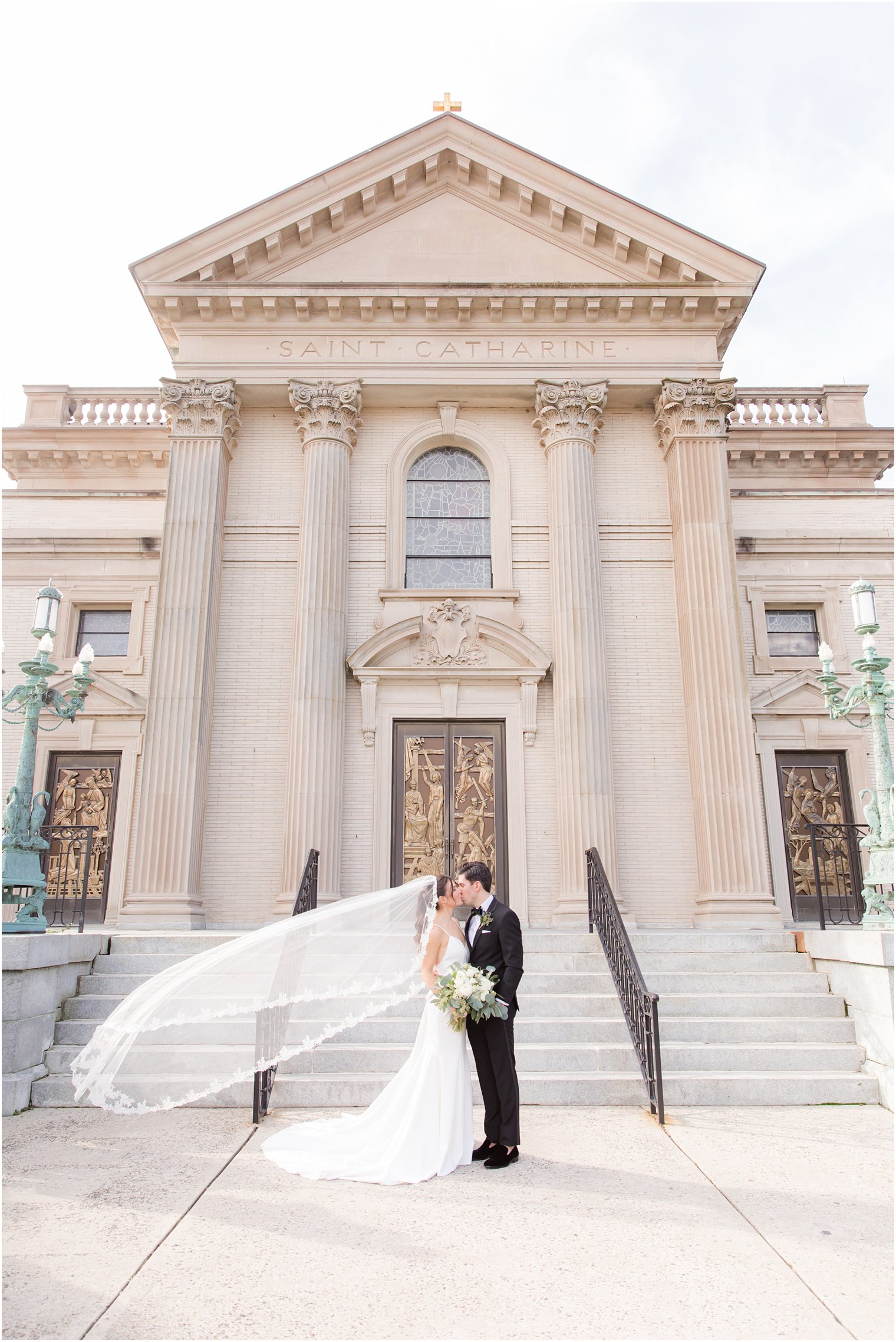bride and groom kiss with bride's veil floating outside St. Catharine's Church in Spring Lake NJ