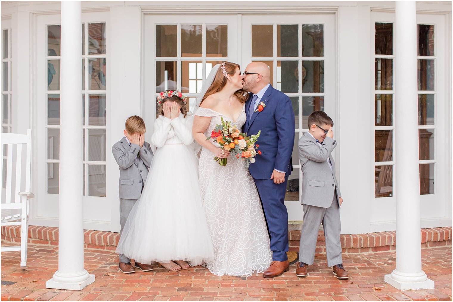 bride and groom kiss while kids hide eyes playfully