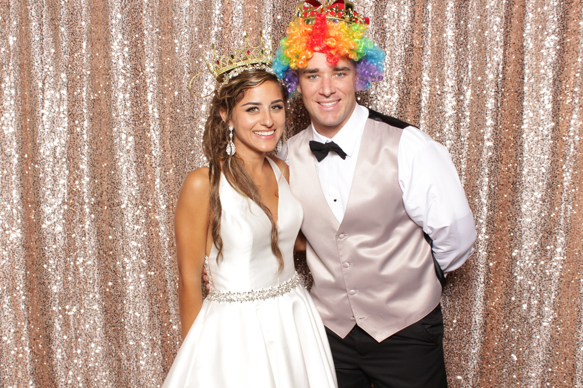 groom in clown wig poses with bride in photo booth