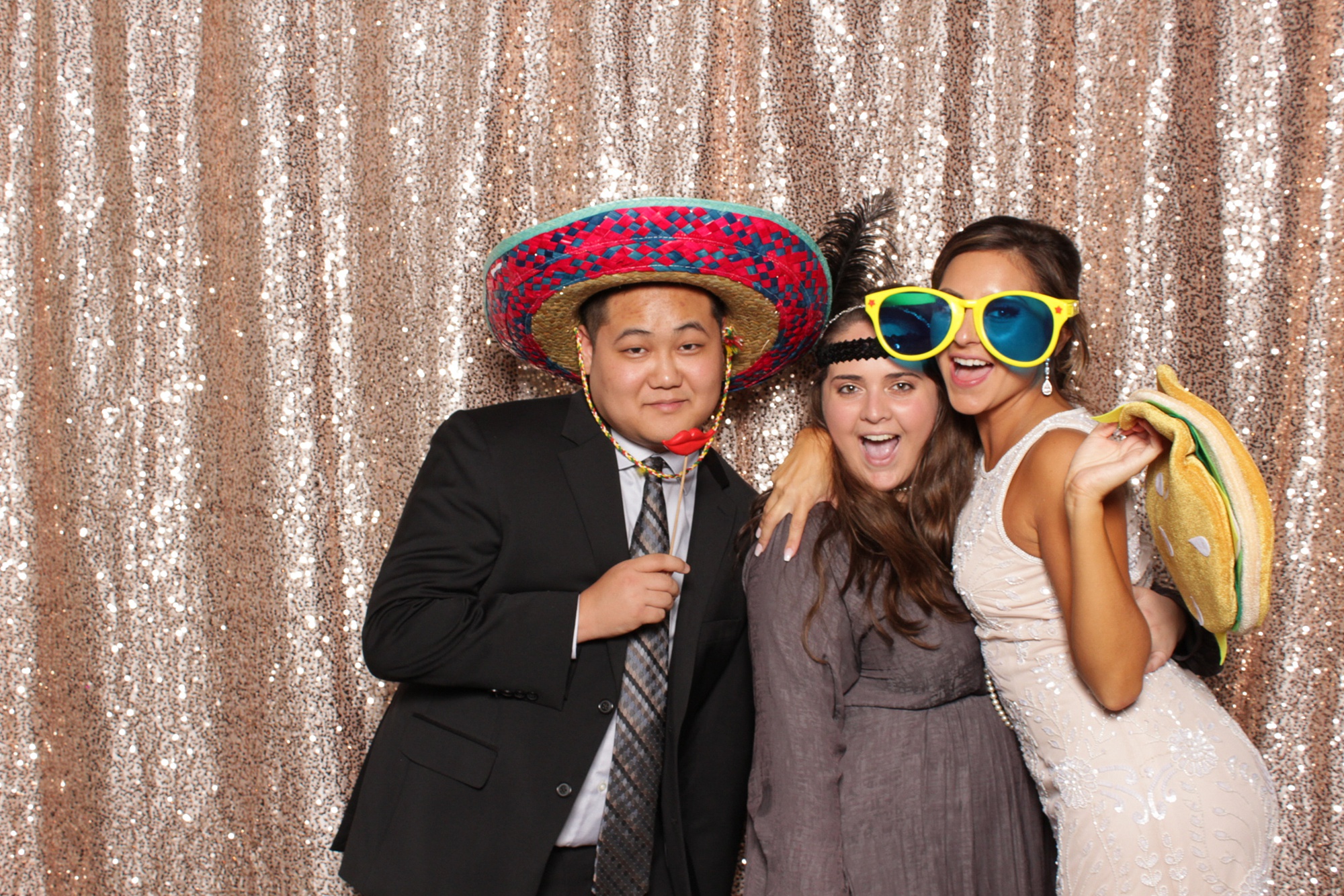 three adults pose in photo booth with sombrero