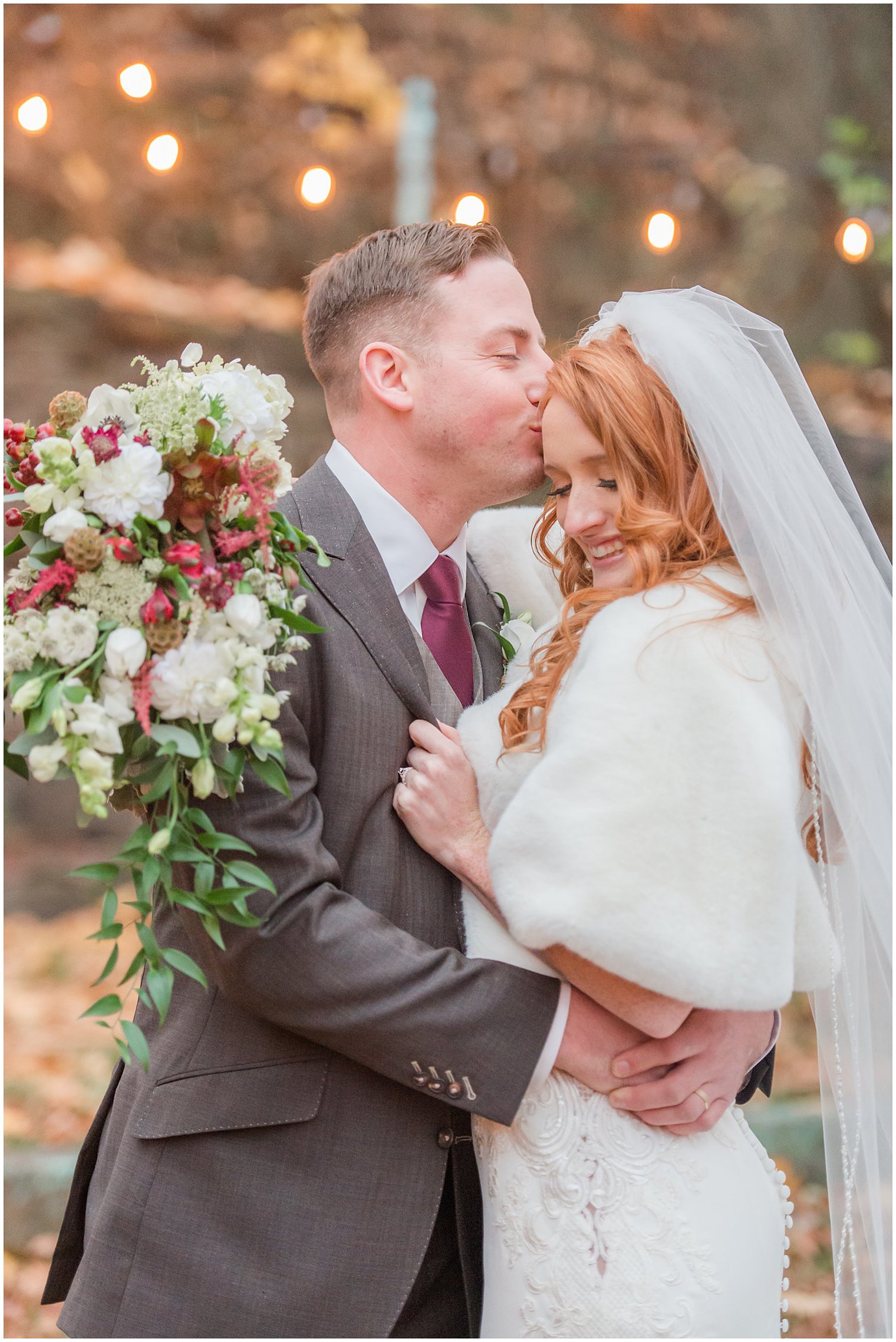 groom kisses bride's forehead while she holds bouquet around his shoulders during Art Factory Studios wedding photos