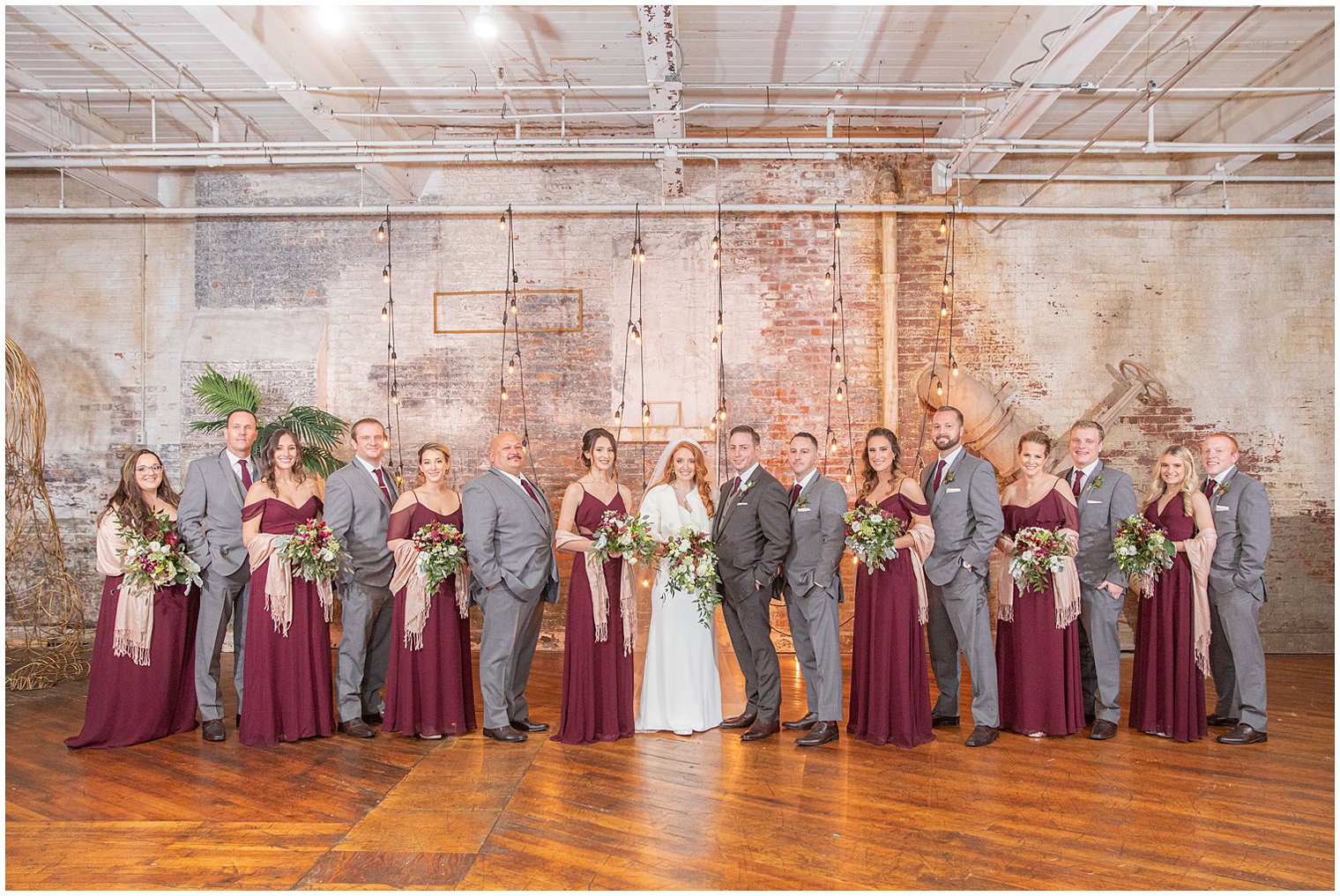 bridal party in grey and burgundy poses by brick wall during Art Factory Studios wedding photos