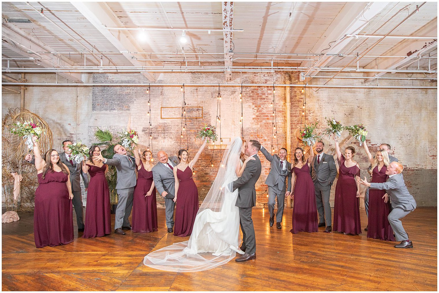 bridal party cheers while groom lifts bride and kisses her