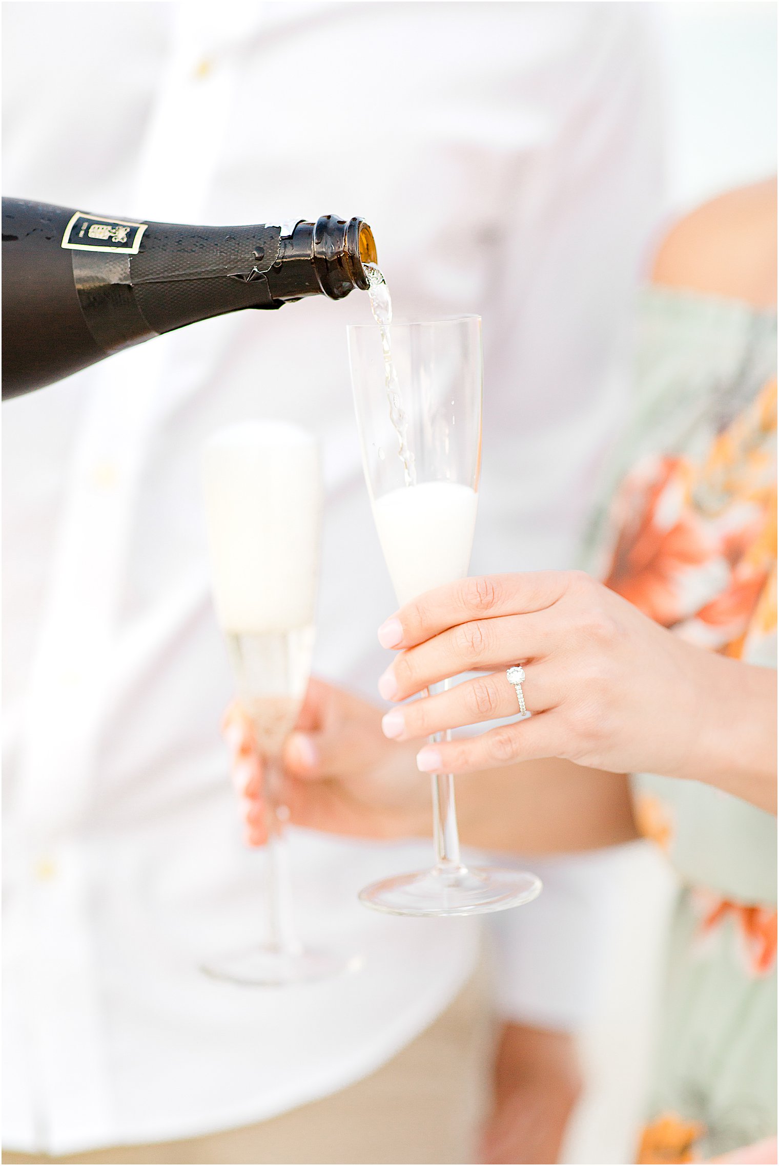 couples brings champagne to toast during engagement photos on the beach