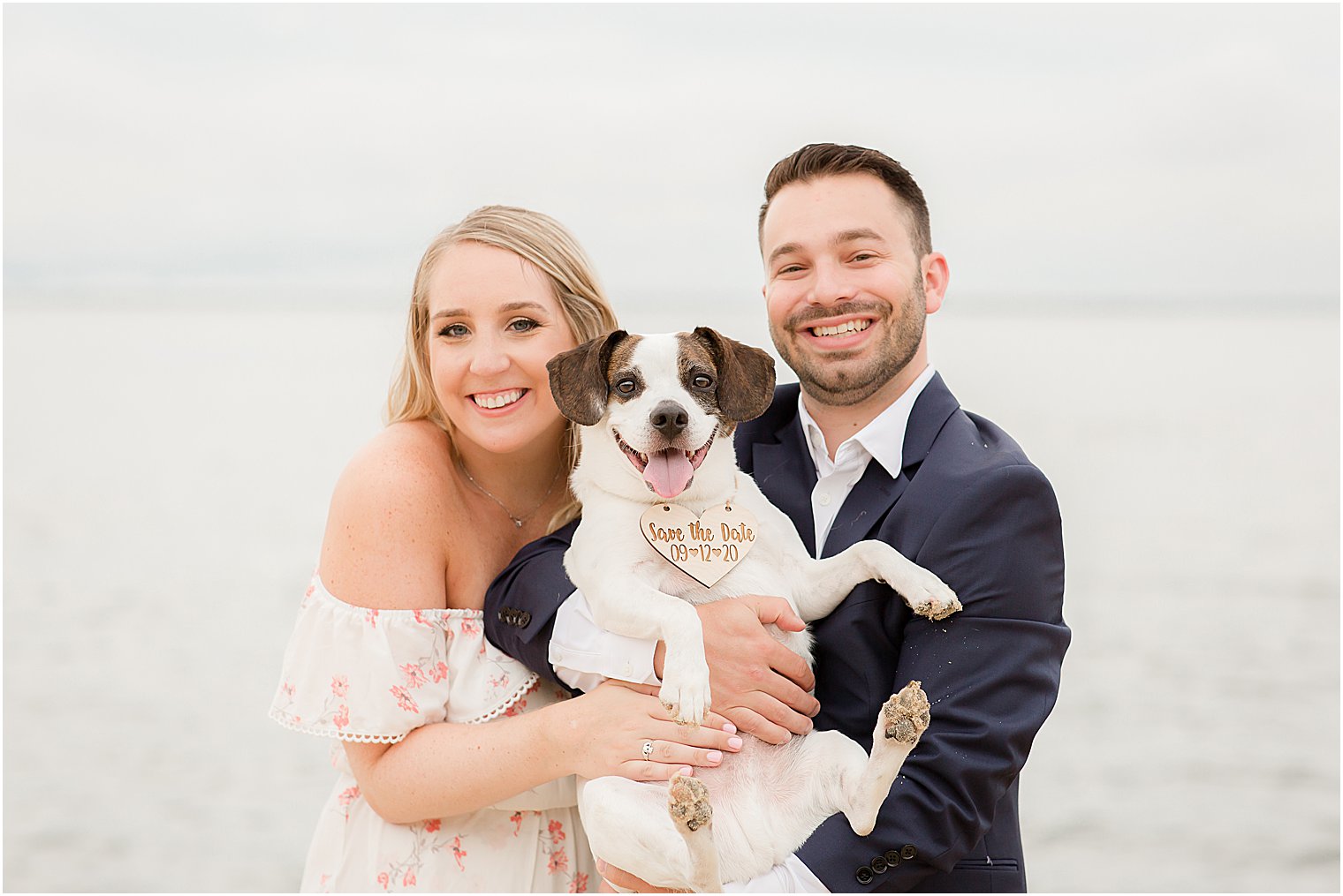engaged couple hugs dog with wooden tag around neck