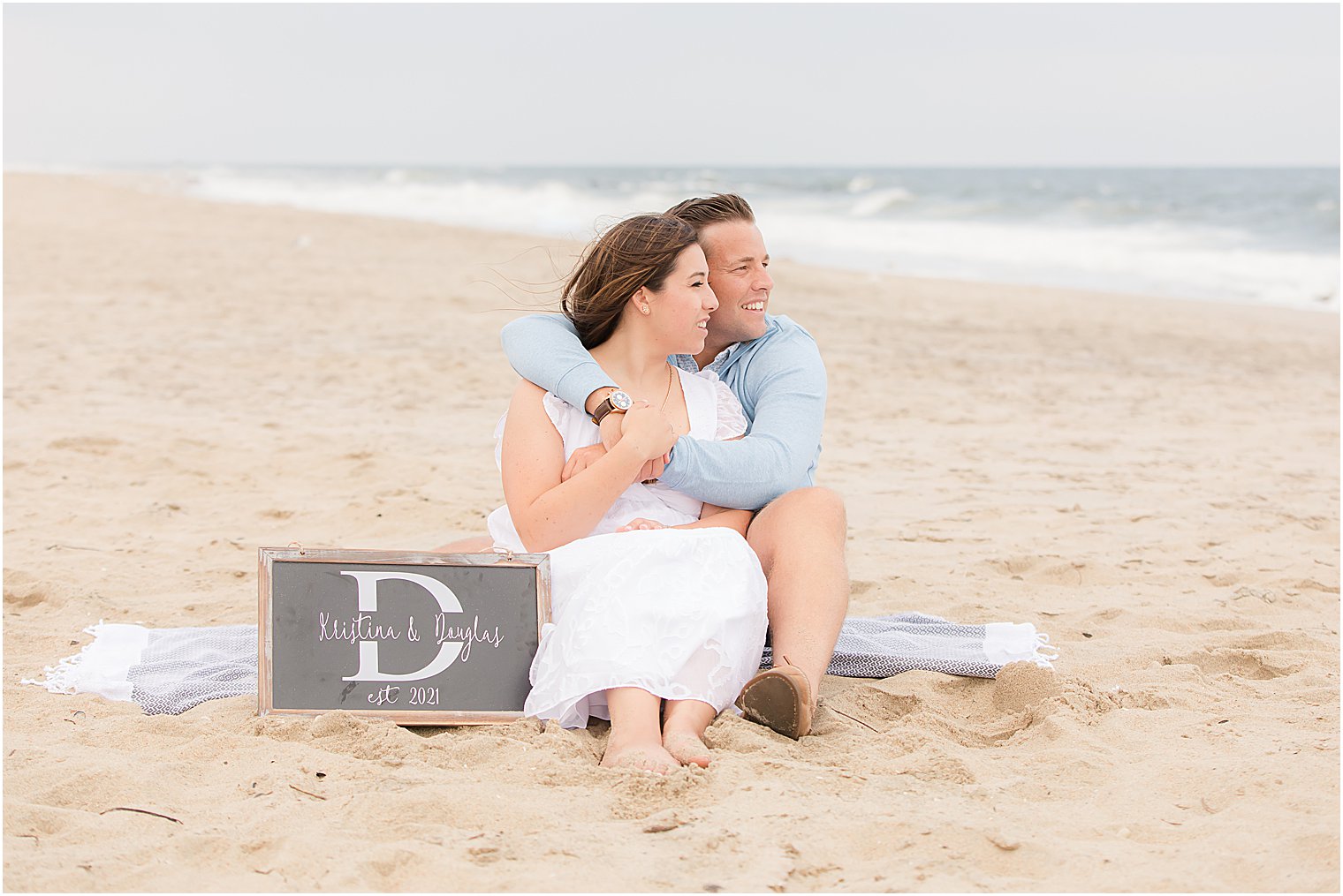 engaged couple snuggles on blanket on the beach