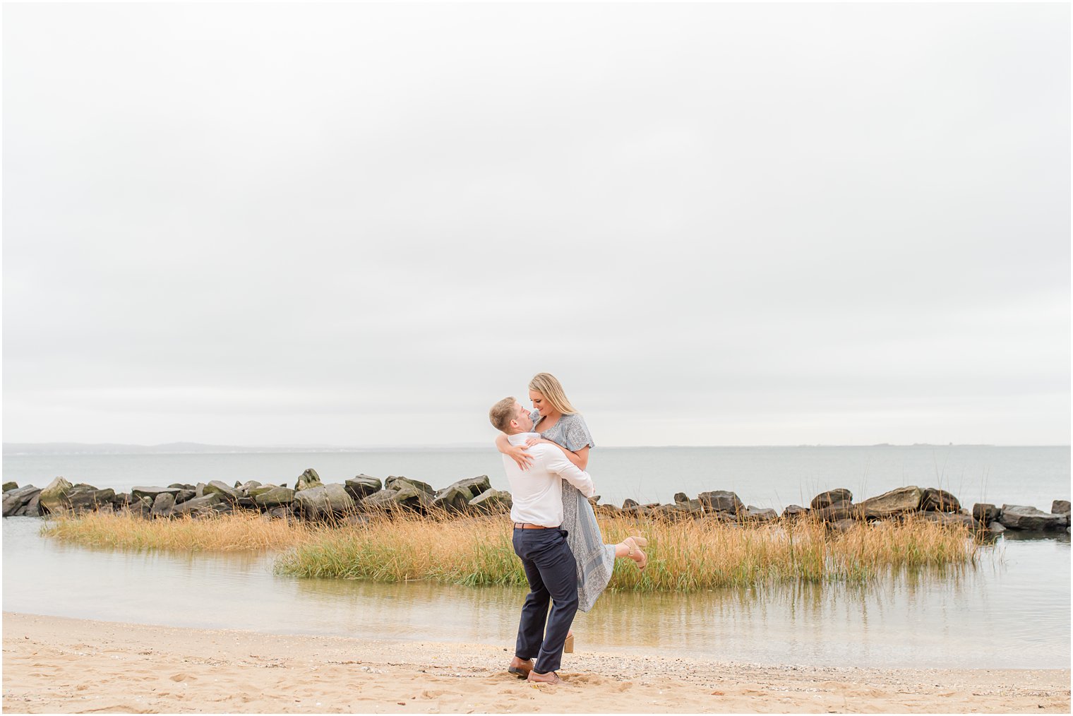 groom lifts bride up during fall engagement photos at Sandy Hook