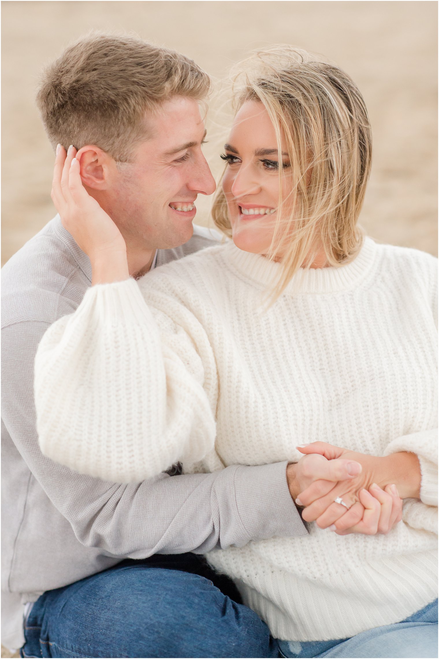 bride and groom snuggle on the beach during winter engagement photos on Sandy Hook Beach