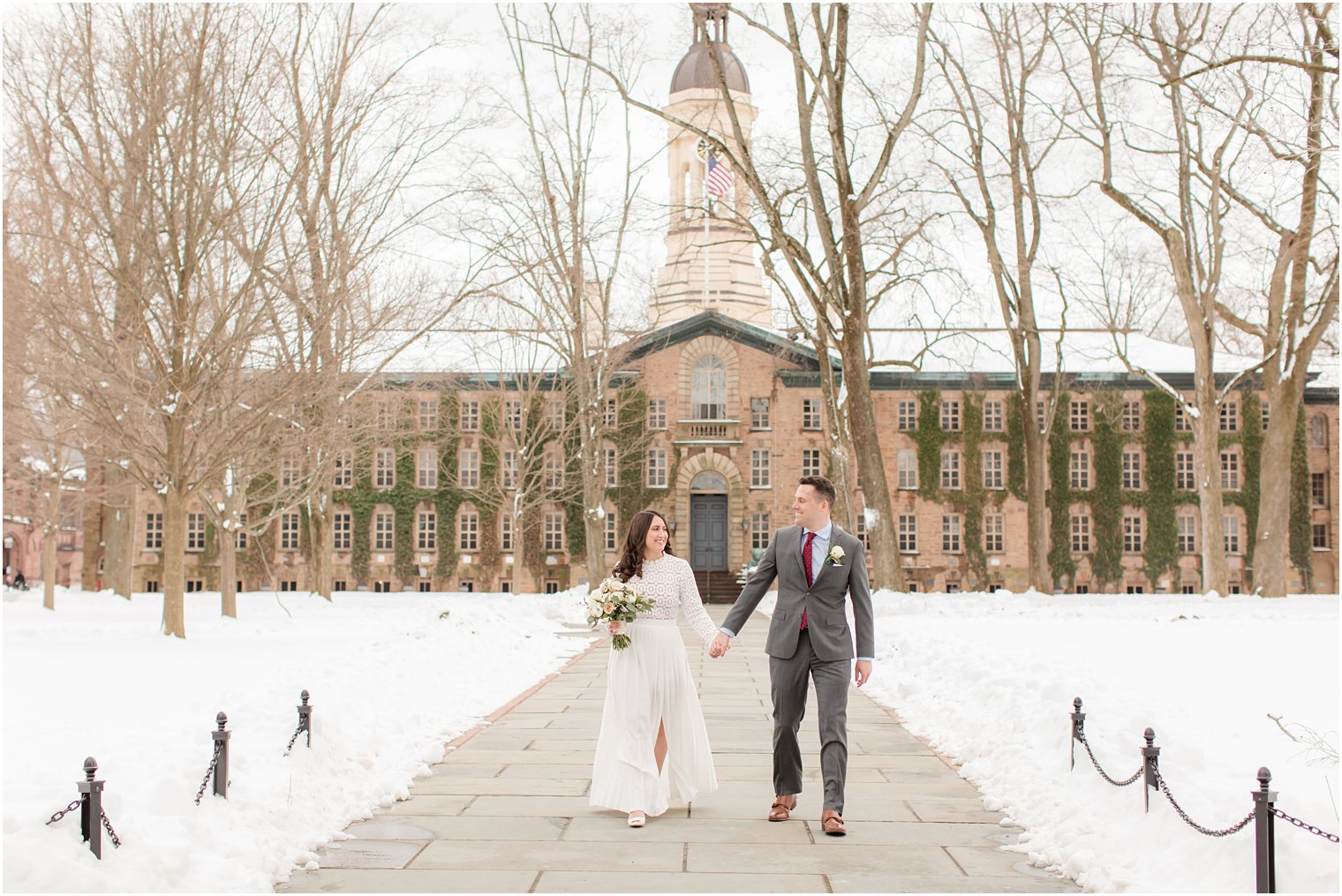 bride and groom hold hands walking in front of Princeton University on snowy day