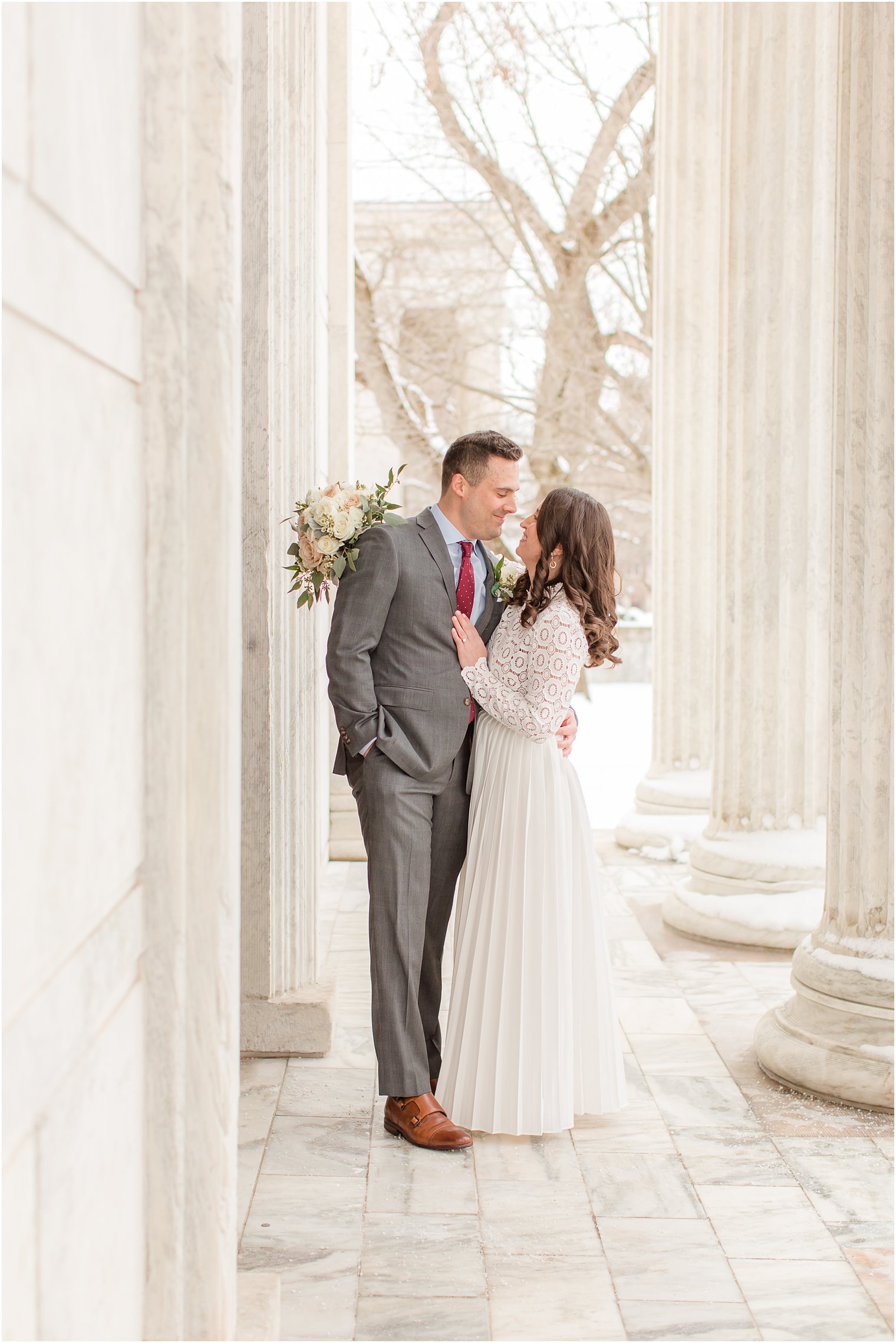 bride and groom hug between pillars at Princeton University building on snowy day