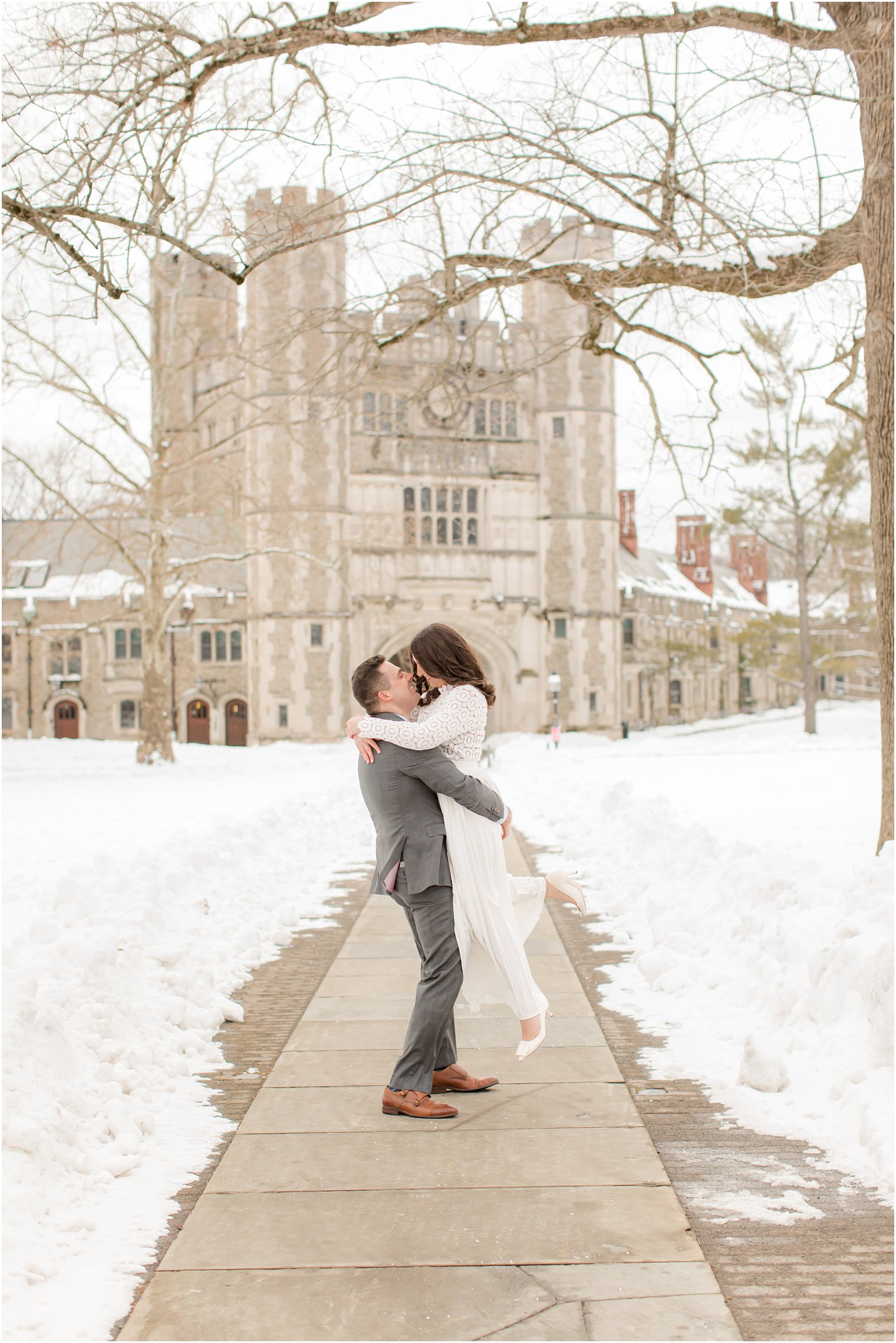 groom lifts bride in front of Princeton University on snowy wedding day