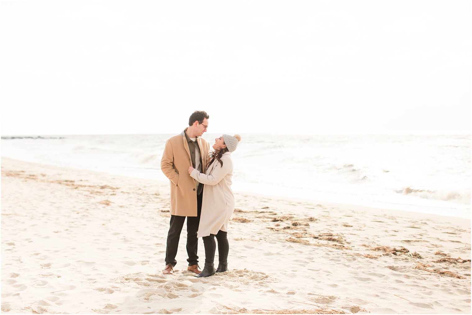 Couple wearing taupe colored coats posing for winter beach shoot in Cape May