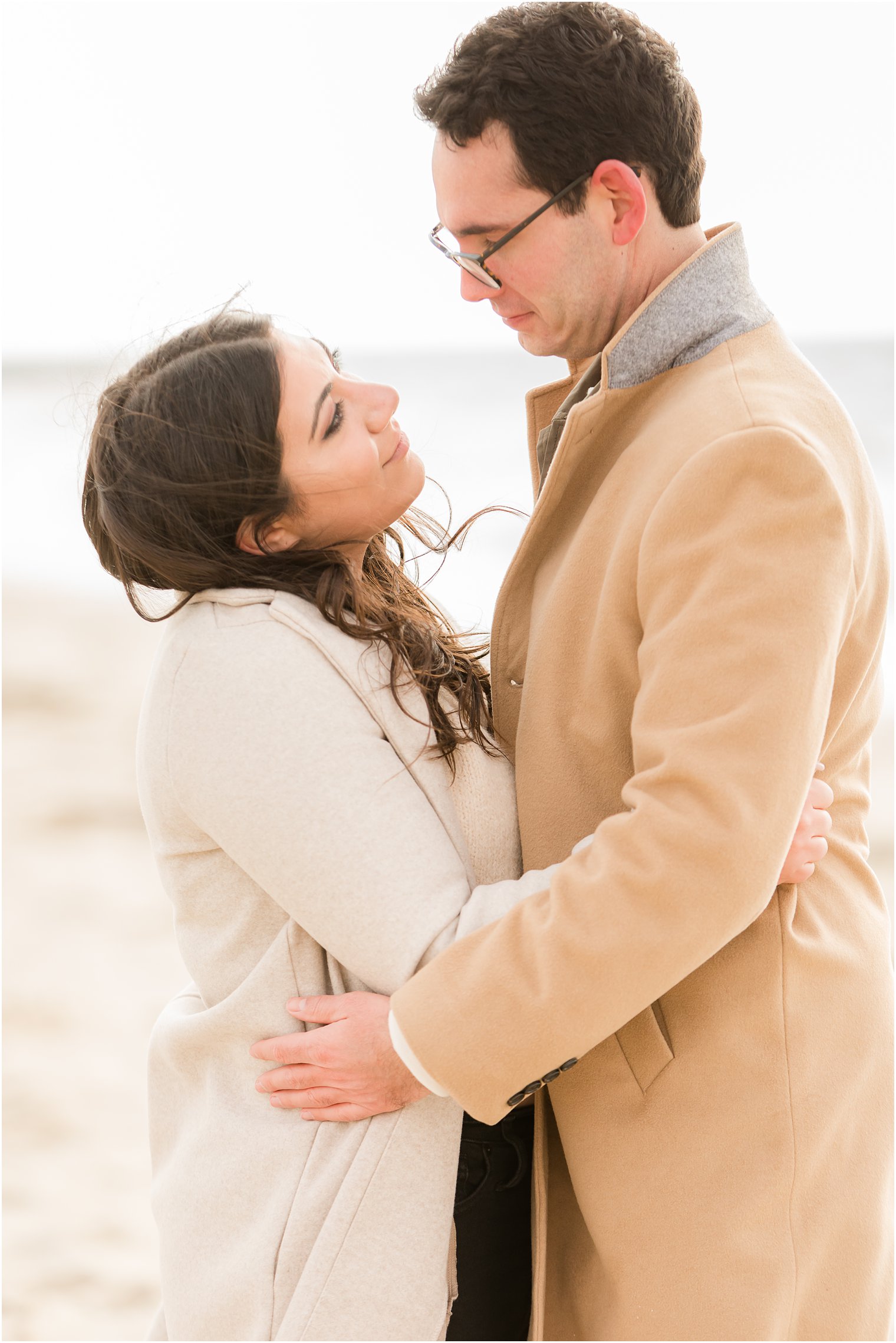 Engaged couple looking lovingly at each other on the beach in the winter