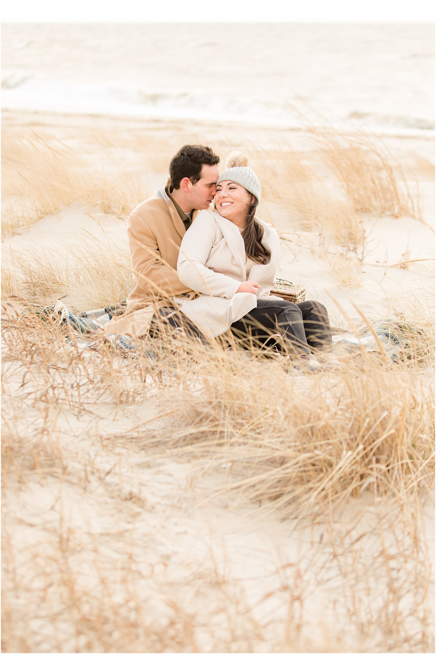 Engaged couple sitting on a blanket in the high grasses at Sunset Beach in Cape May