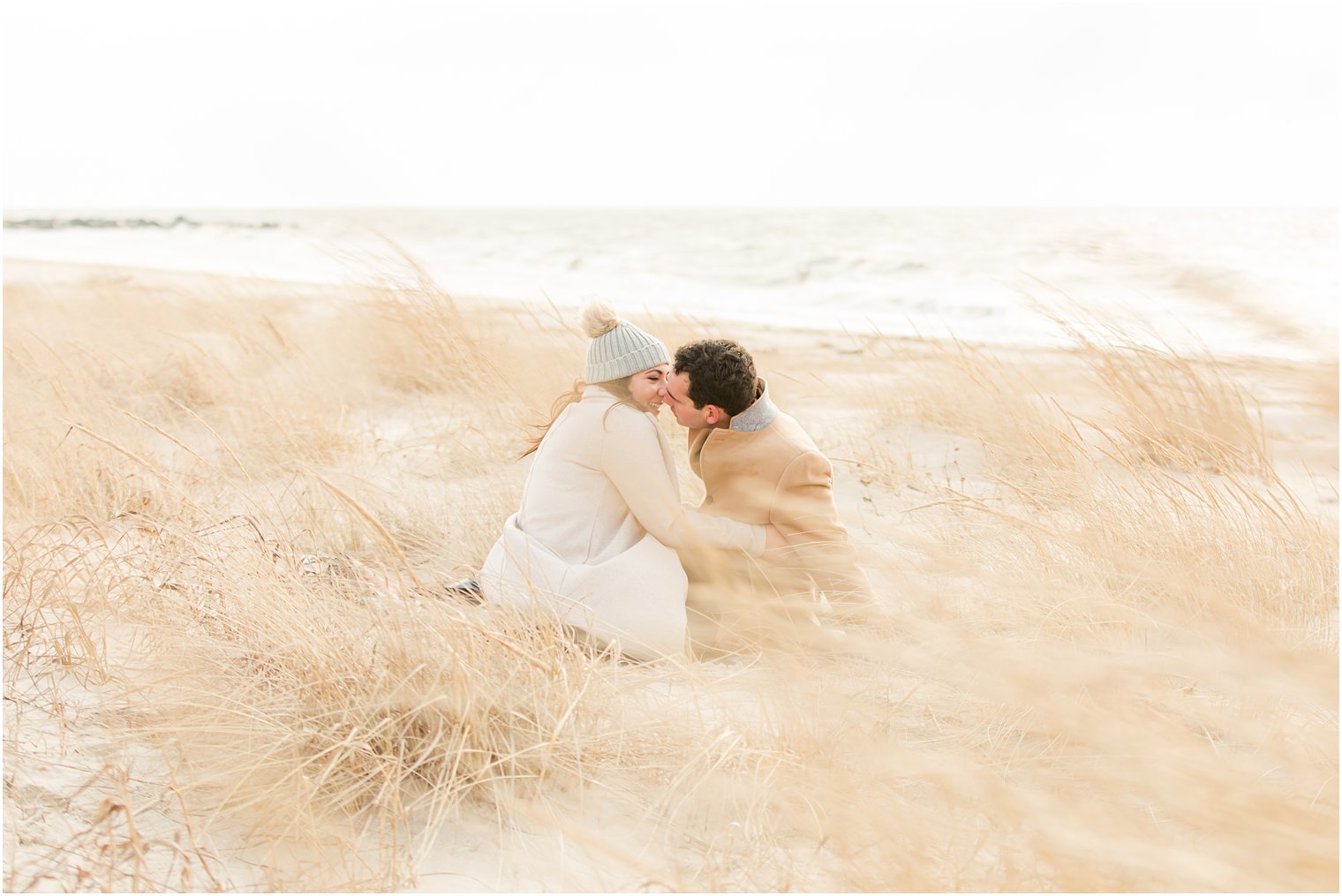 Engaged couple sitting on a blanket in the sand dunes and kissing 
