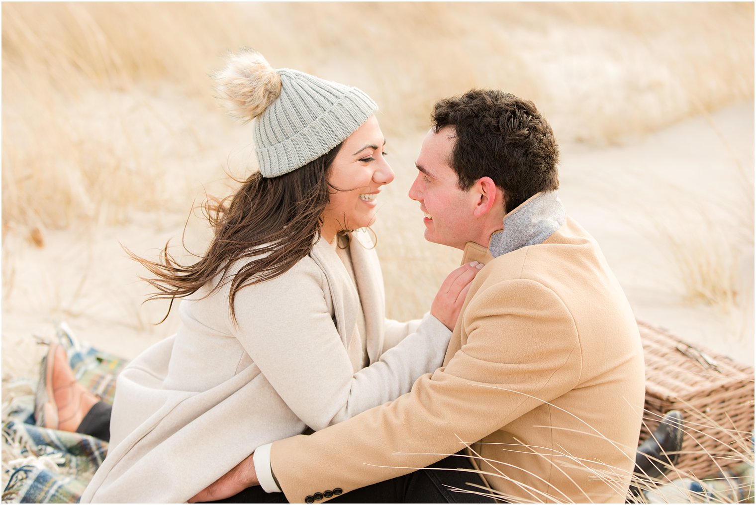 Engaged couple sitting facing each other on the beach in the winter