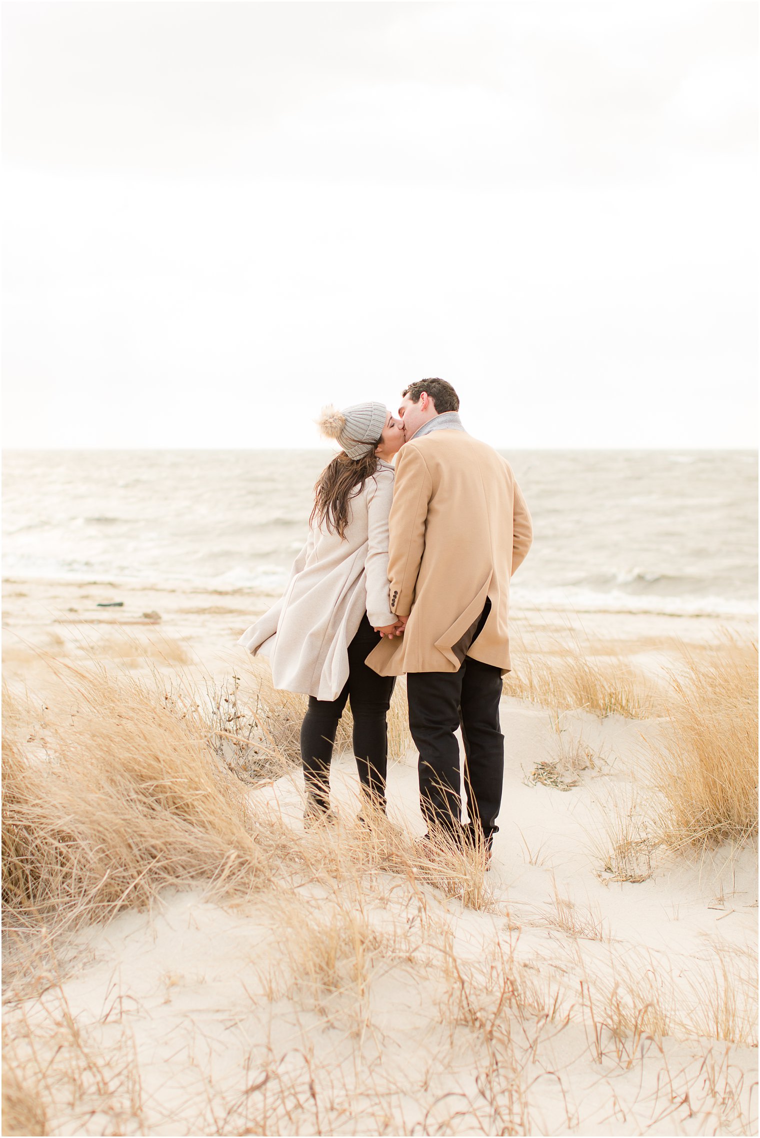 Engaged couple holding hands and kissing on the beach in the winter